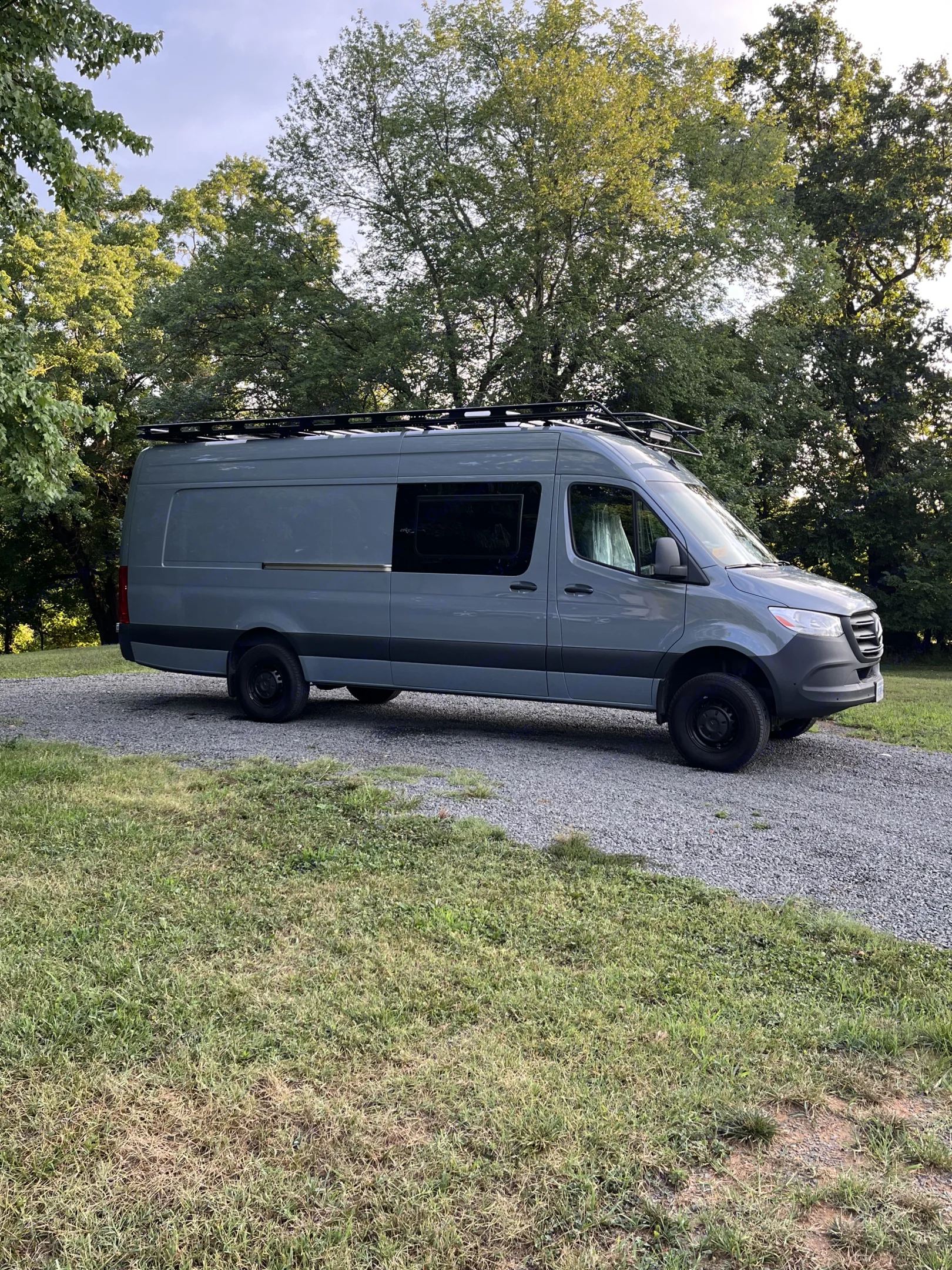 Gray Mercedes-Benz Sprinter camper van, perfect RV rental, parked on a gravel drive with lush trees. Ready for your next adventure.. Mercedes benz Sprinter 2022