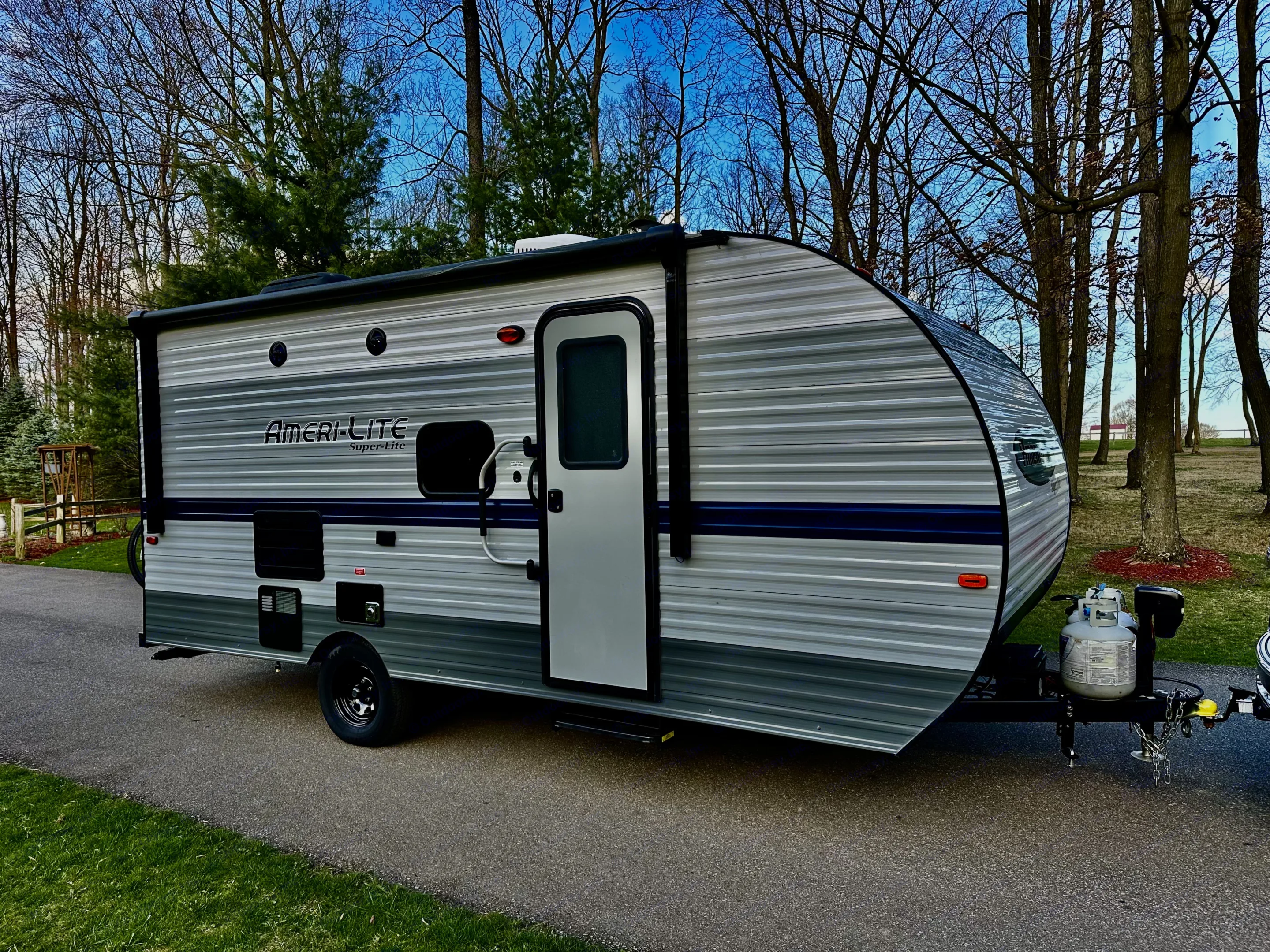 This Ameri-Lite Super-Lite travel trailer, ideal for an rv rental, is parked on a paved lot surrounded by trees, ready for adventure.. Gulf Stream Ameri-Lite Super Lite 2021