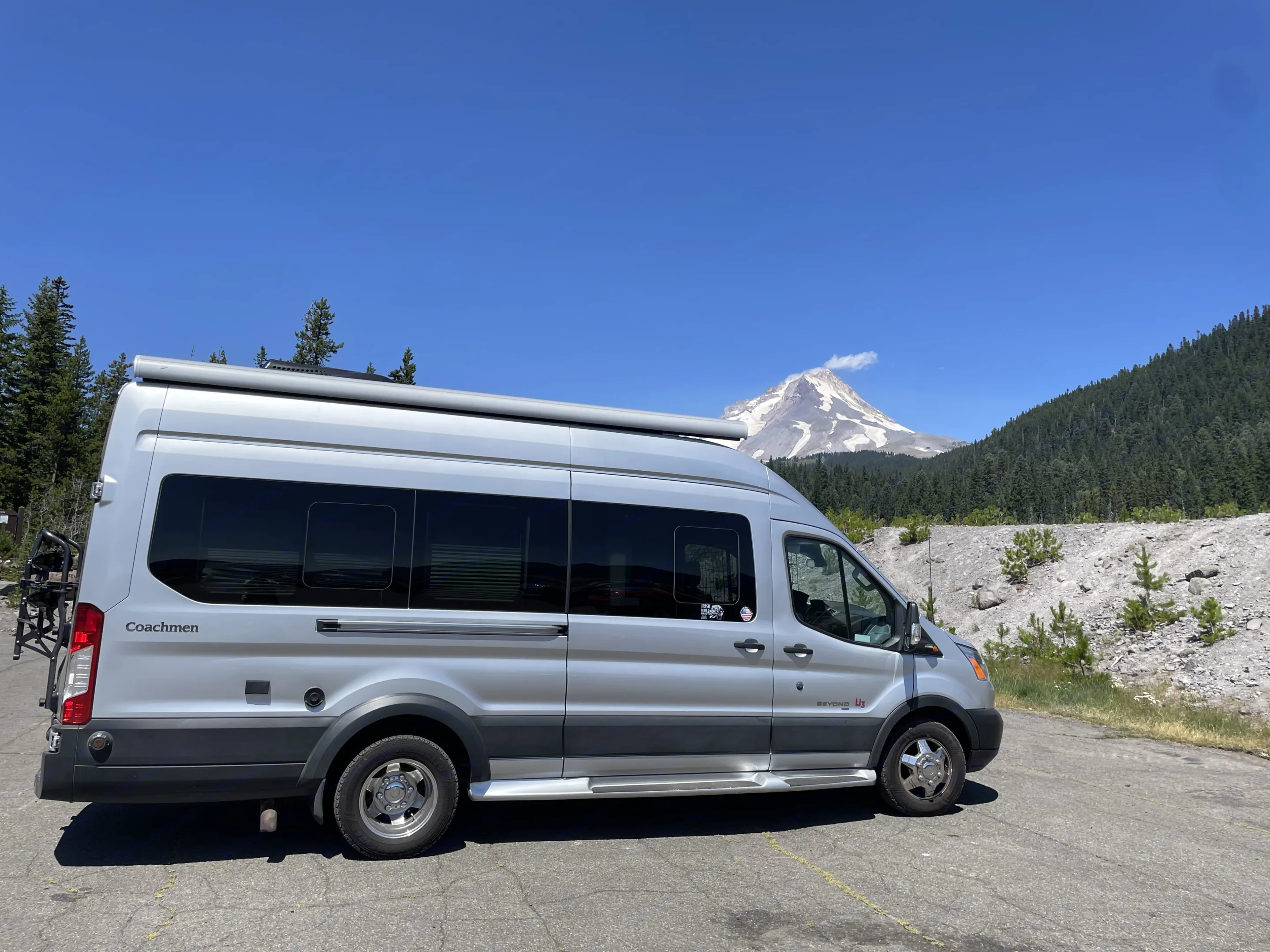 Silver Coachmen Beyond RV rental van facing a majestic snow-capped mountain, lush forest, and clear blue sky.. Coachmen Beyond 22D 2020