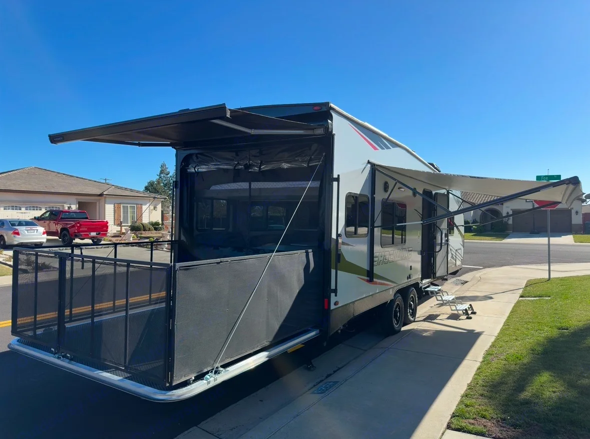 This RV rental, a toy hauler, is set up with a rear patio deck and extended awnings on a sunny suburban street.. Forest River Shockwave 2021