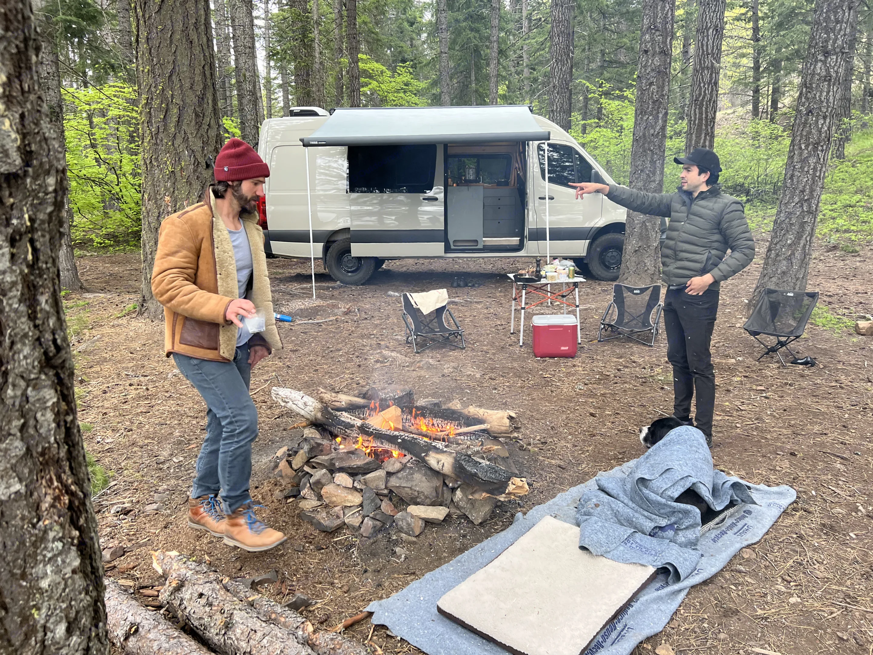Enjoying van life with an RV rental! Two men and their dog camp in a forest with a campfire and Sprinter van.. VanCraft VanCraft Class B 2023