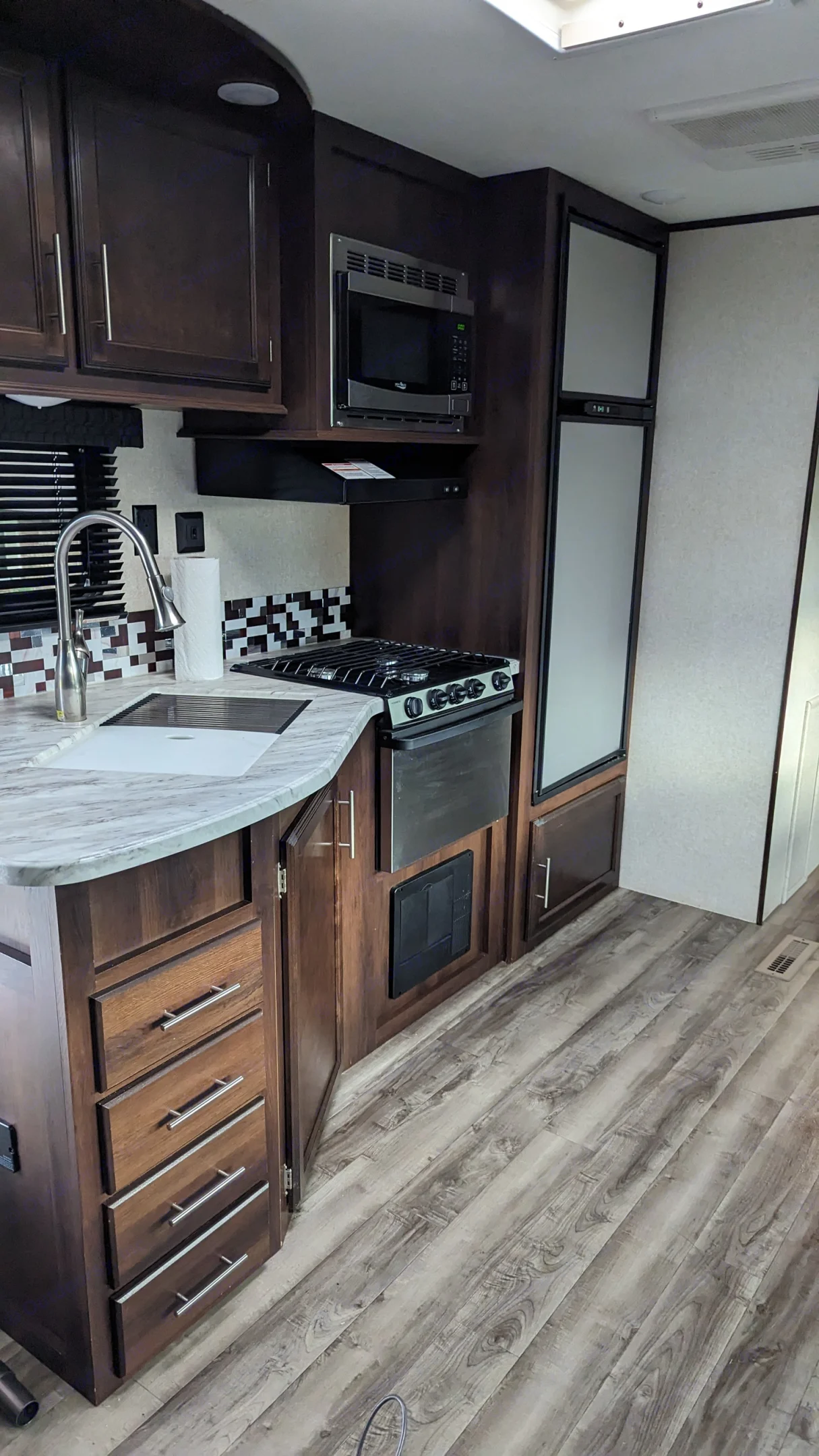 Modern RV rental kitchen featuring a sink, stove, microwave, refrigerator, dark wood cabinets, and sleek flooring.. Jayco Jay Flight 2019
