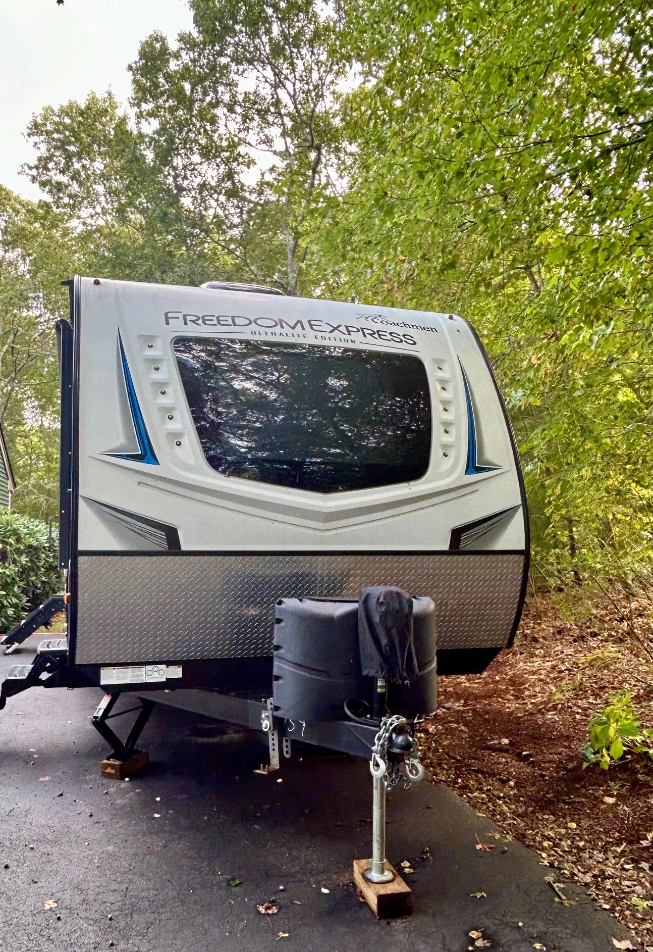 A white Coachmen Freedom Express travel trailer, ideal for an rv rental, is parked on asphalt with trees in the background. Features a large front window.. Coachmen Freedom Express 287 BHDS 2021