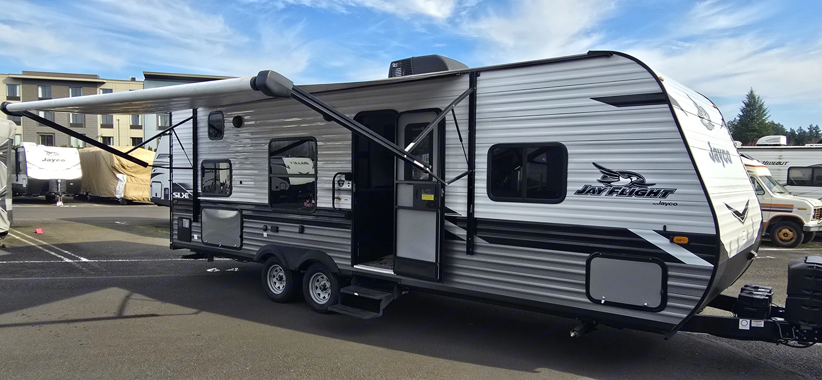 This grey Jayco Jay Flight travel trailer RV rental with extended awning and open door, is parked outdoors.. Jayco Jay Flight SLX 2022