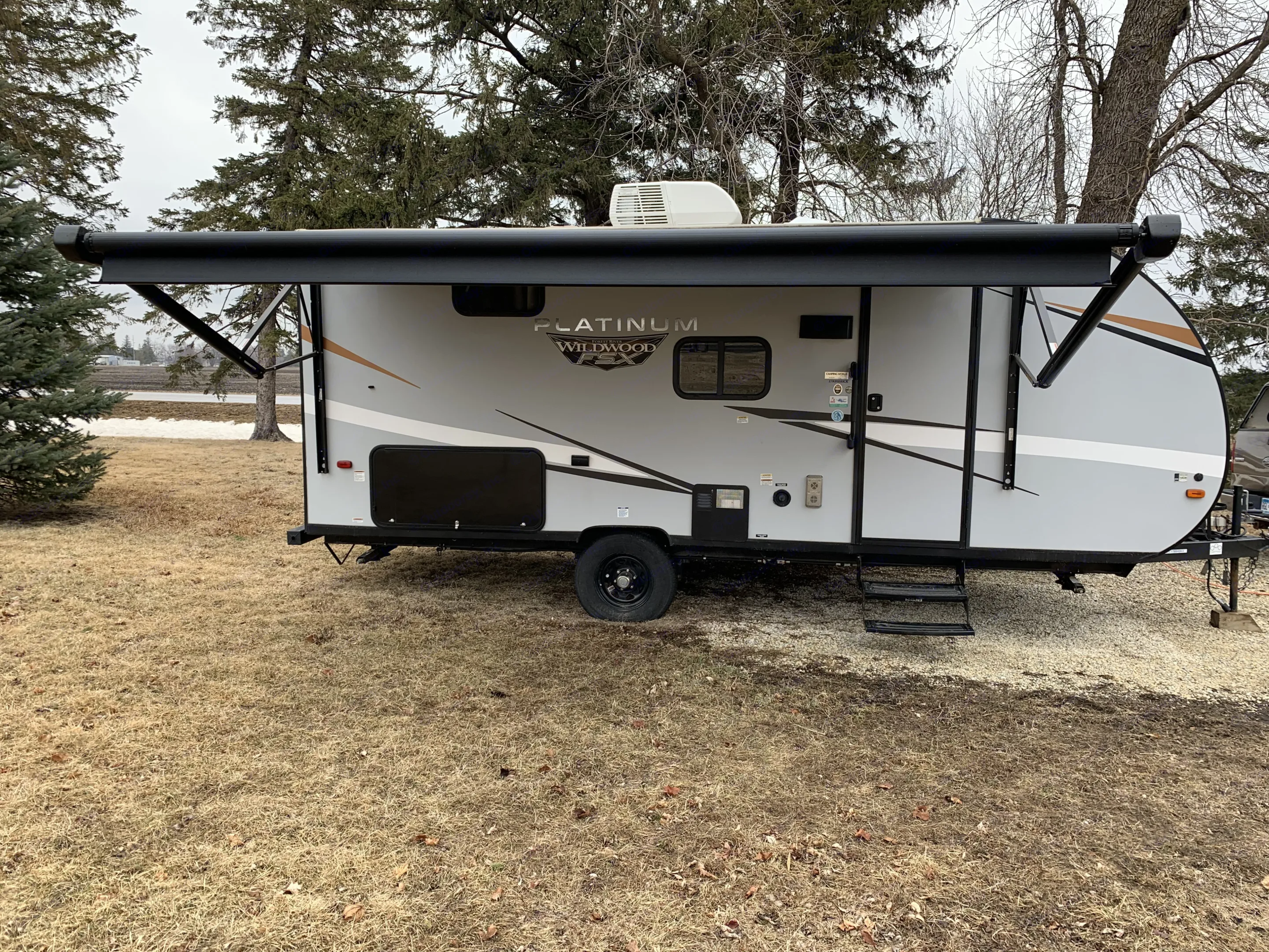 Modern gray Wildwood FSX travel trailer parked in nature with awning deployed, ideal for your RV rental getaway.. Forest River Wildwood FSX Plantium 2022