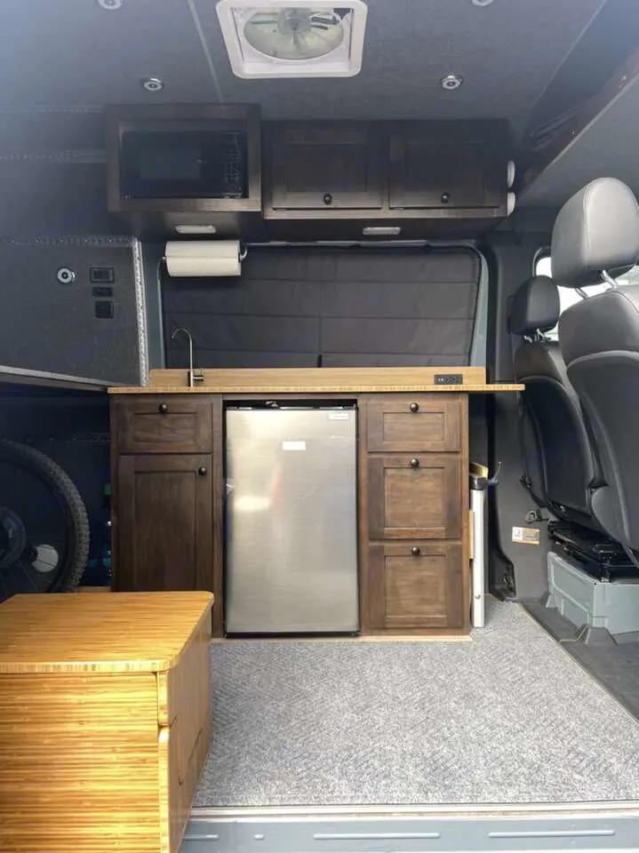 Inside this rv rental van conversion: a practical kitchenette with fridge, microwave, and smart storage options.. Mercedes 313 CDi 4 X 4 Sprinter 2020