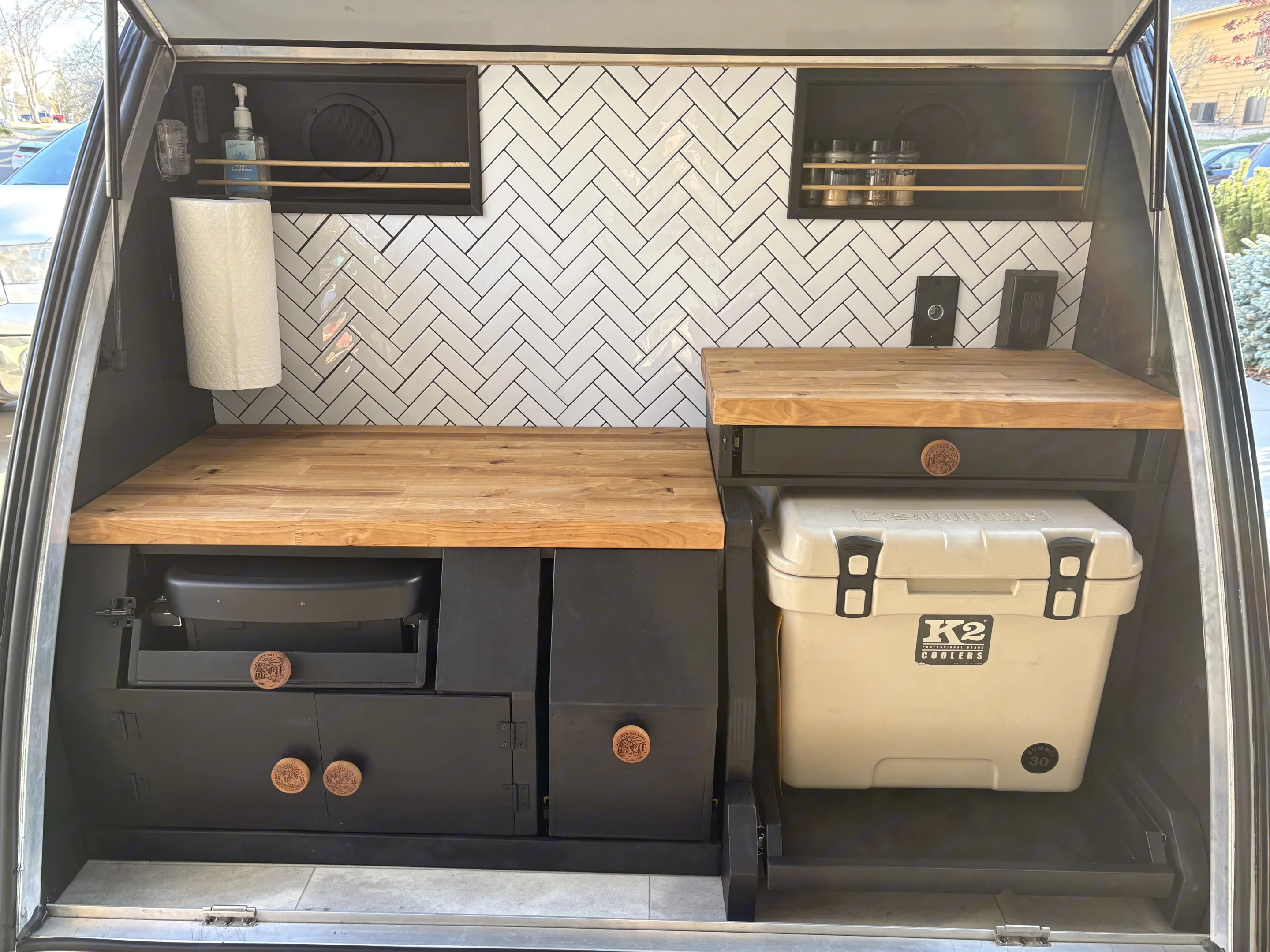 A compact, stylish RV rental kitchen featuring wood countertops, herringbone tiles, and built-in cooking gear and cooler.. Braxton Creek Free Solo 2022