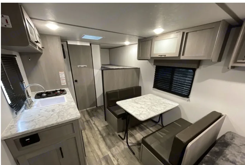 Inside an RV rental: a bright interior with a kitchen, dinette that converts to a bed, and bunk beds. Dutchmen Coleman Lantern LT 2023