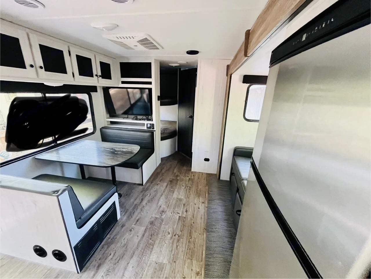 This RV rental interior offers a spacious dinette, TV, and bunk beds, with a full-size refrigerator on the right. Modern and functional.. Heartland RVs Trail Runner 2023