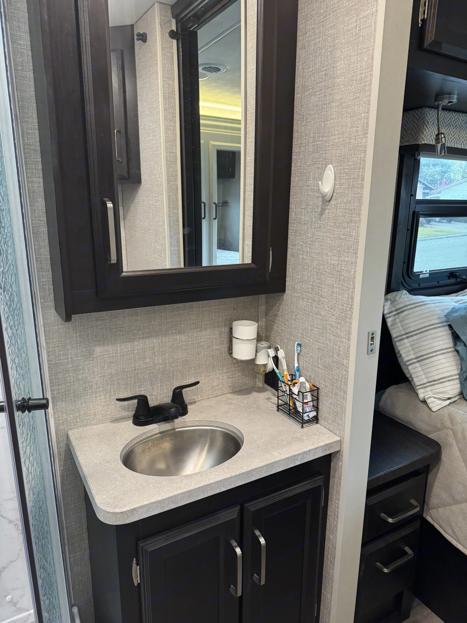 This RV rental's compact bathroom features a vanity, sink, mirror, and organized toiletries for convenience.. Jayco Greyhawk 2023