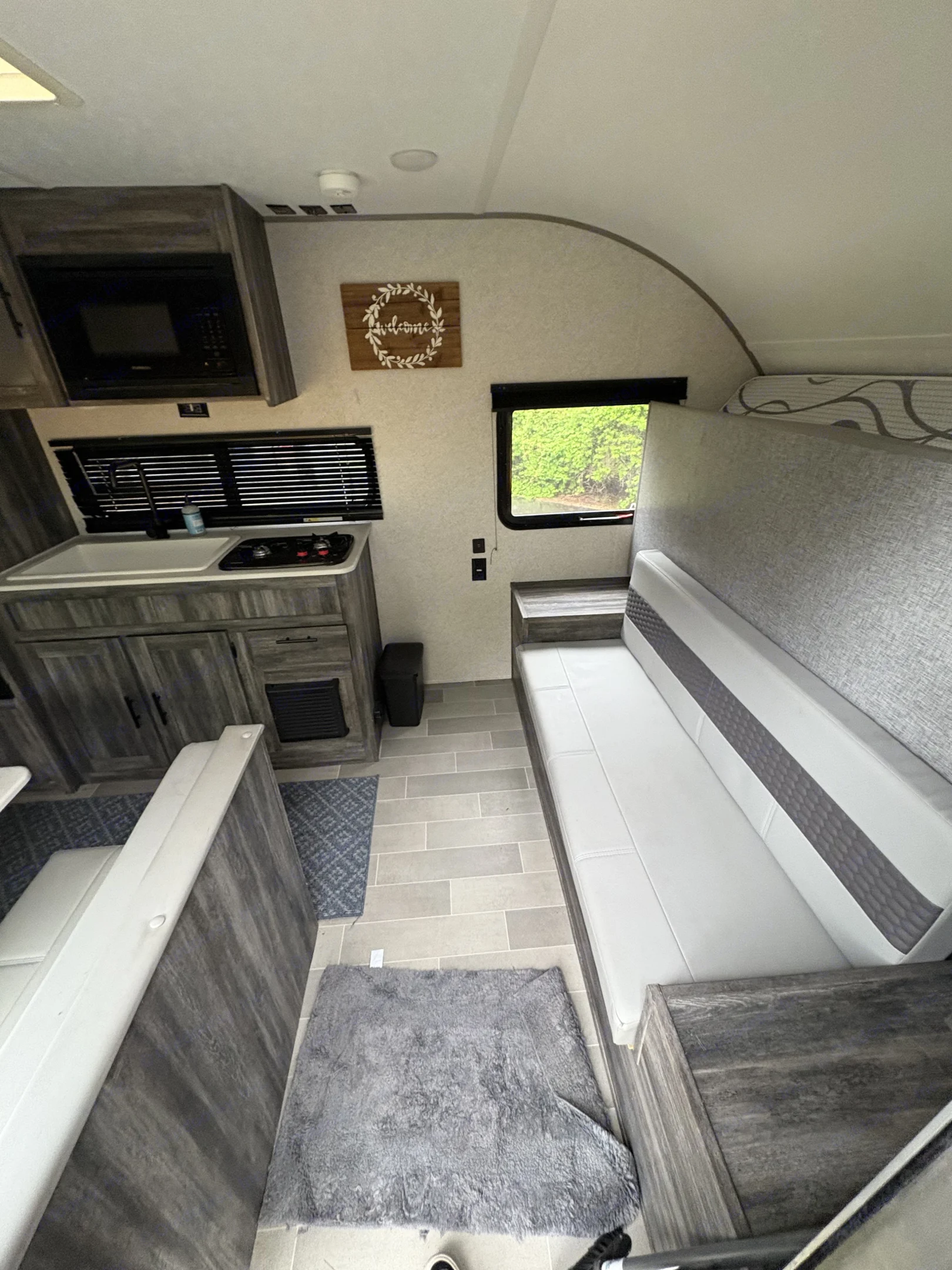 This RV rental interior showcases a compact kitchenette with a sink and stove, along with a comfortable dinette. Modern grey tones throughout.. Forest River Wildwood FSX 2019