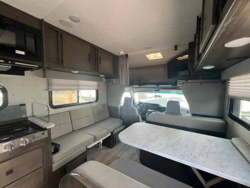 Spacious RV rental interior featuring a kitchen with microwave, comfy sofa seating, and a dining area, ideal for road trips.. Coachman Leprechaun 2022