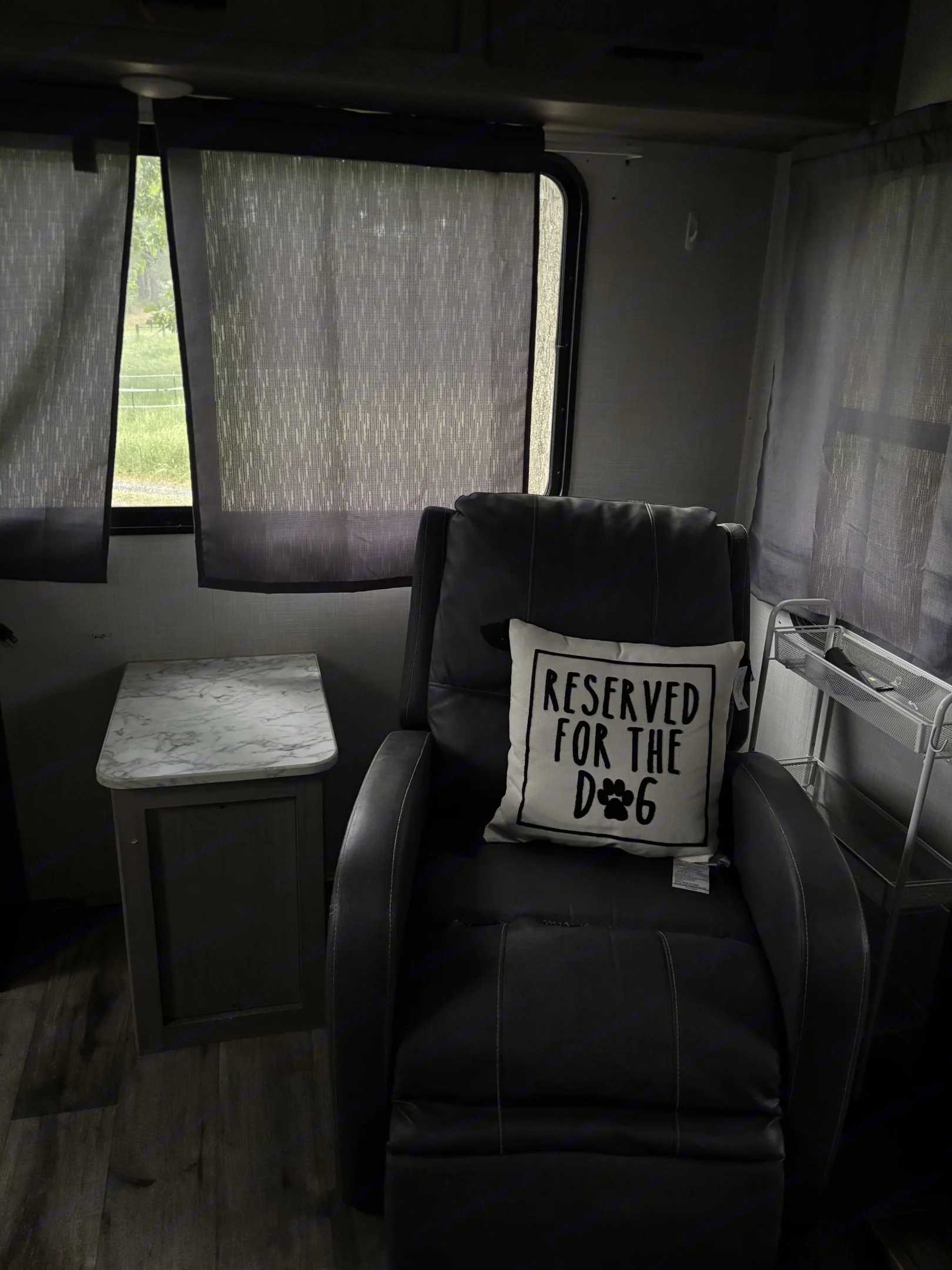 Cozy RV rental interior featuring a comfy recliner with a 'RESERVED FOR THE DOG' pillow, side table, and nature view.. Dutchmen Coleman Light 2022