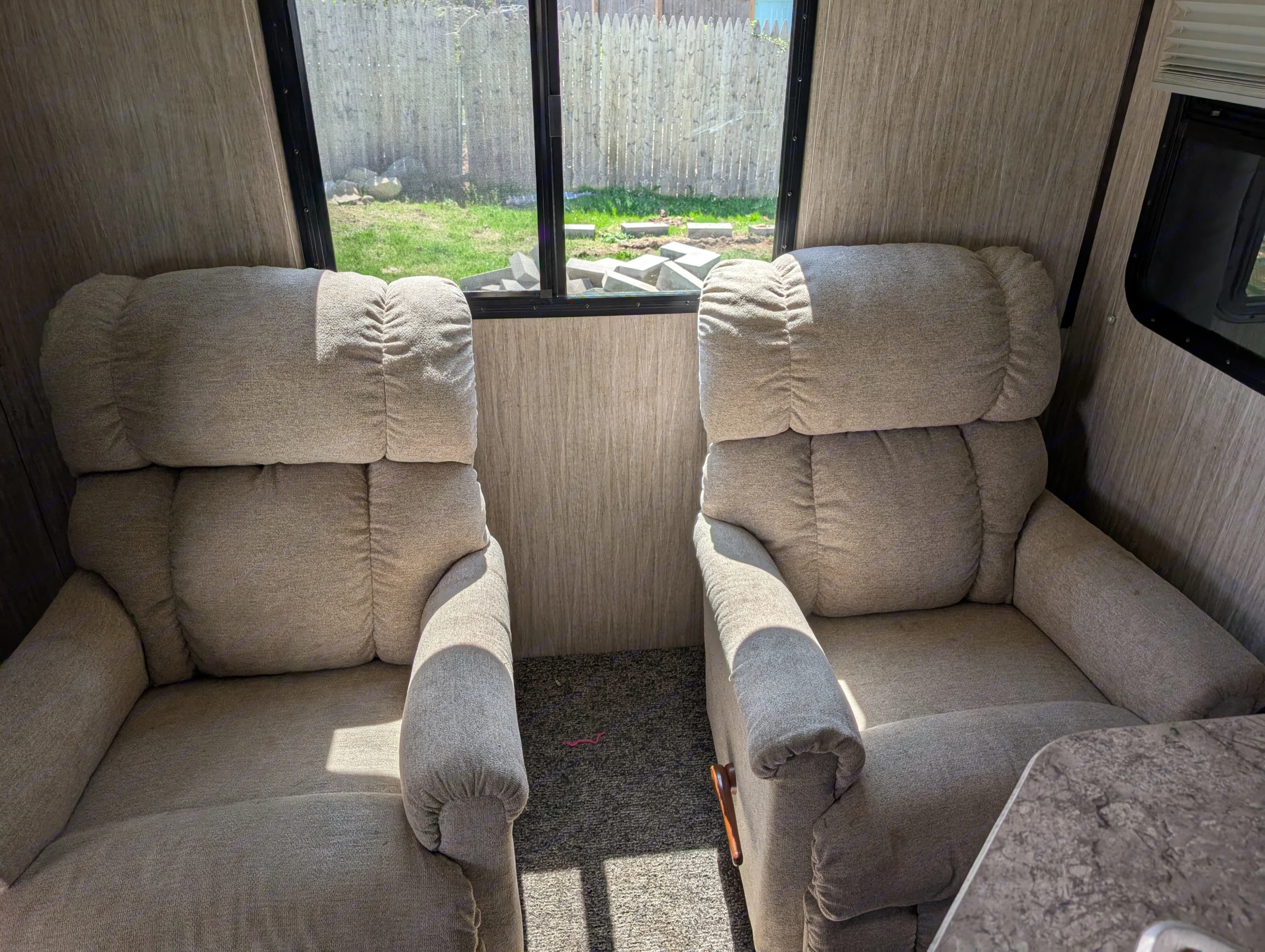 Cozy RV rental interior with two comfortable recliners, offering a sunny view of the outdoors through large windows.. Heartland RVs Sundance 2019