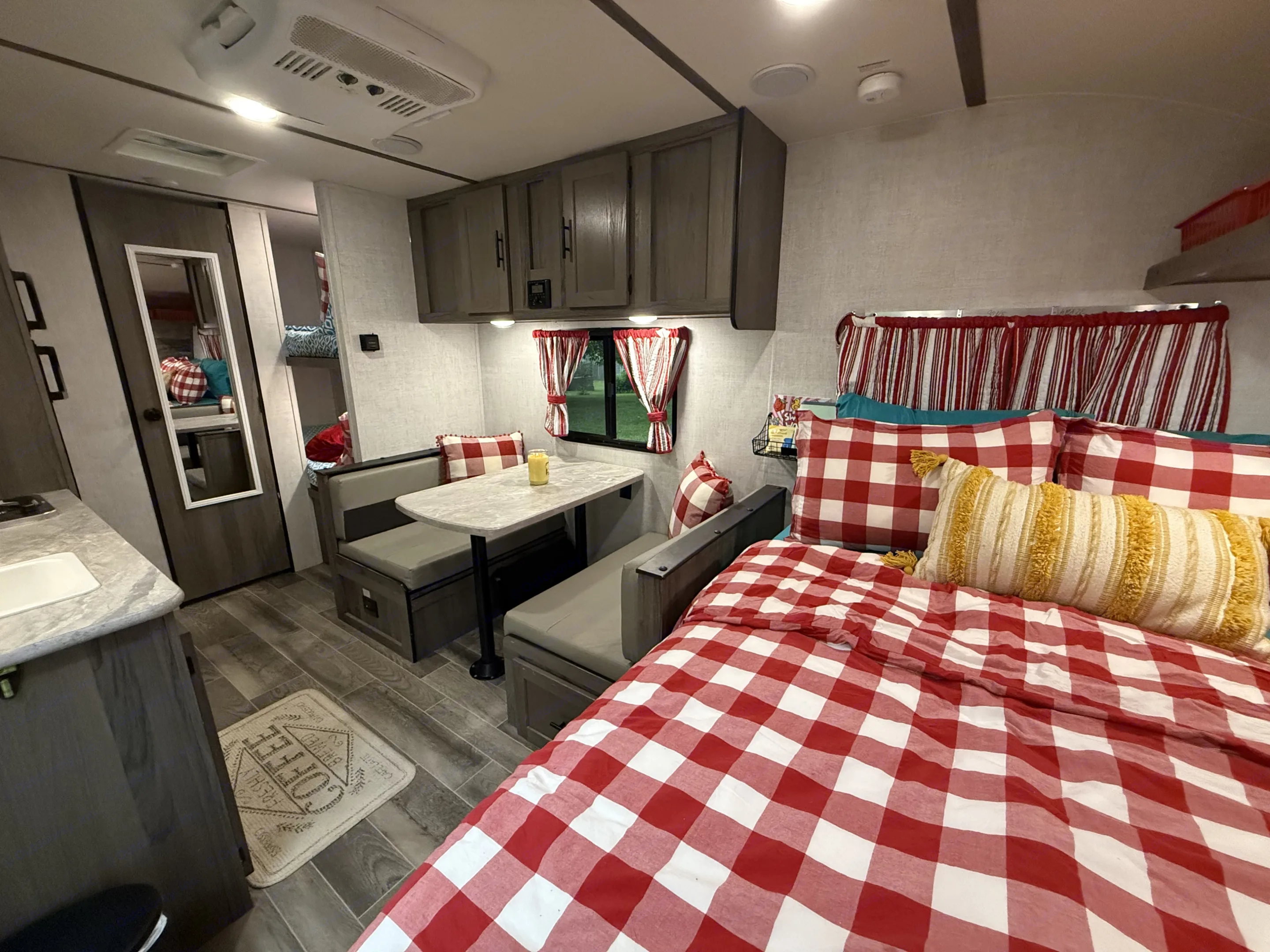 Inside a colorful RV rental: kitchen, dining, and bedroom with red & white decor. Comfortable travel accommodations for your trip.. Gulf Stream Ameri-Lite Super Lite 2021