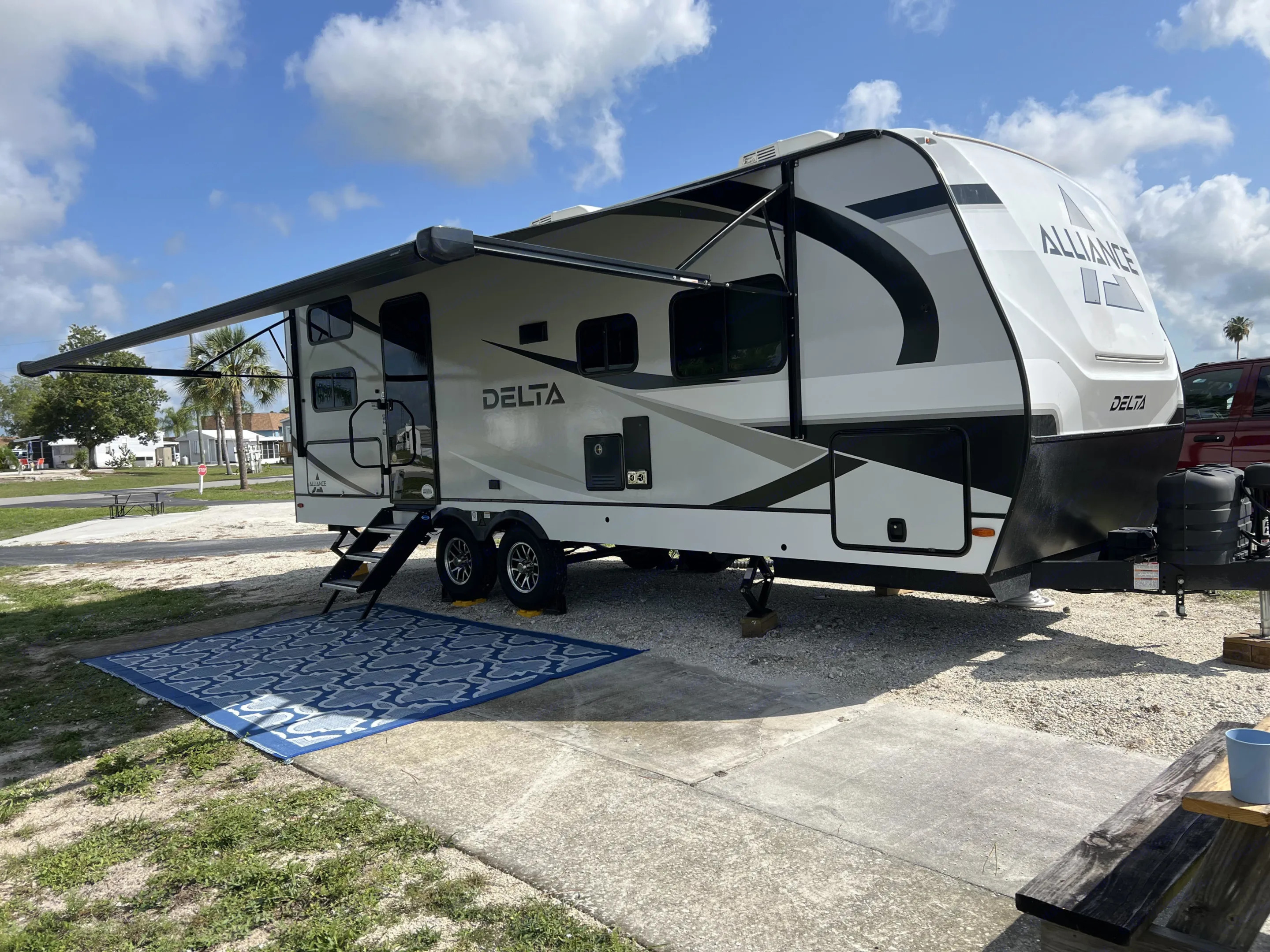 Experience comfort in this Alliance Delta RV rental. Parked at a sunny campsite with extended awning and outdoor rug.. Alliance Delta 251BH 2024