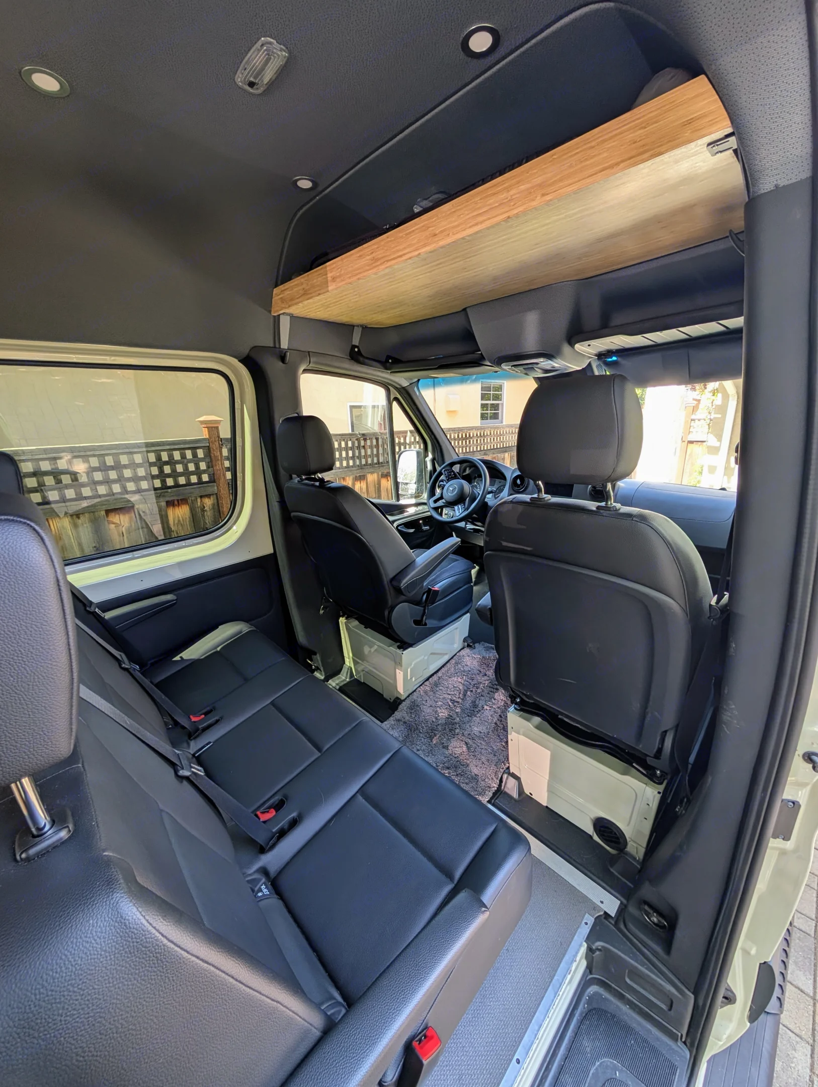 Interior of an RV rental van featuring multiple rows of black leather seating and a wooden overhead storage shelf.. Mercedes-Benz Sprinter 2020