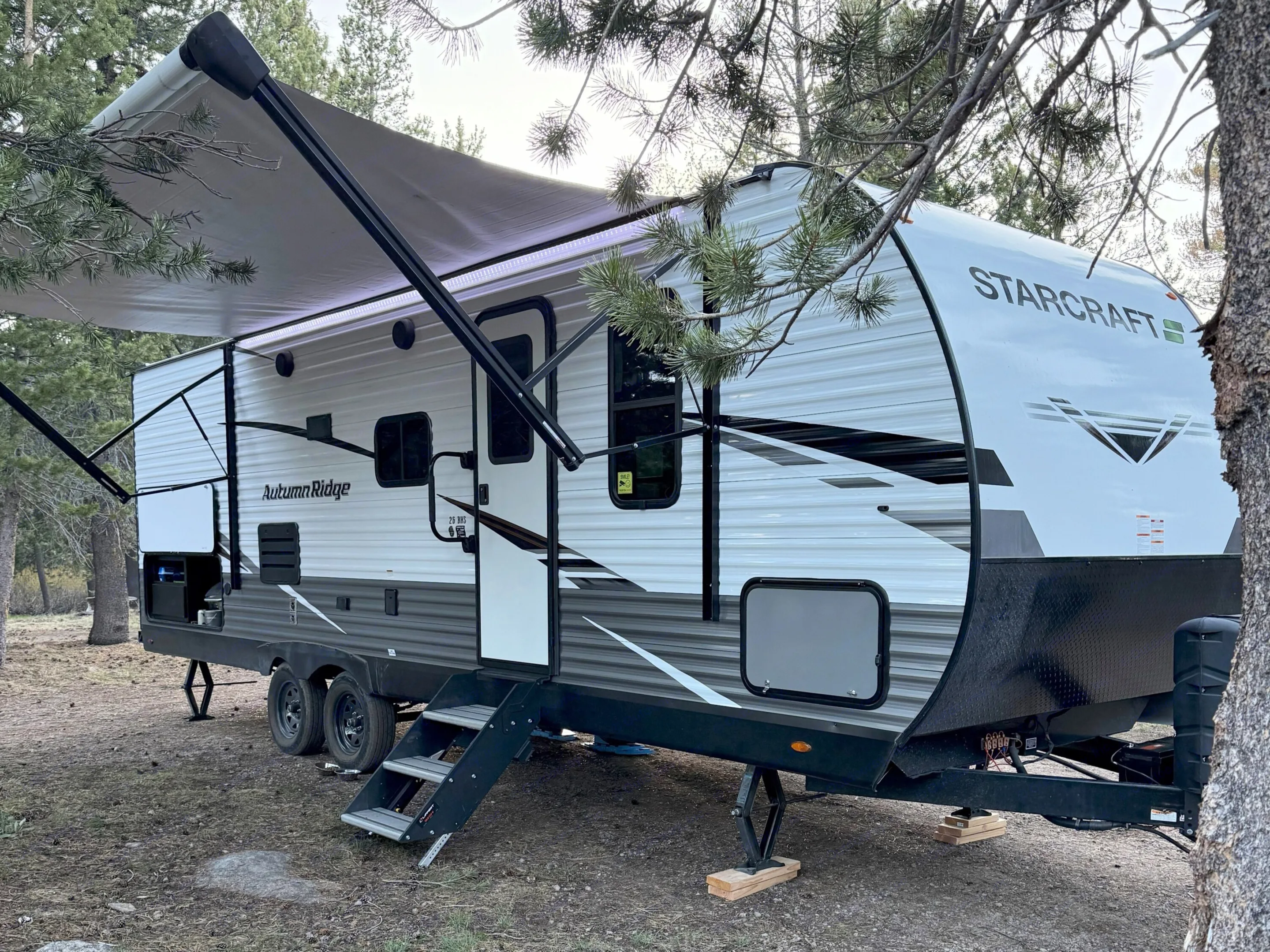 This RV rental, a Starcraft Autumn Ridge travel trailer, is set up for camping under an awning in a wooded area.. Starcraft Autumn Ridge 2023
