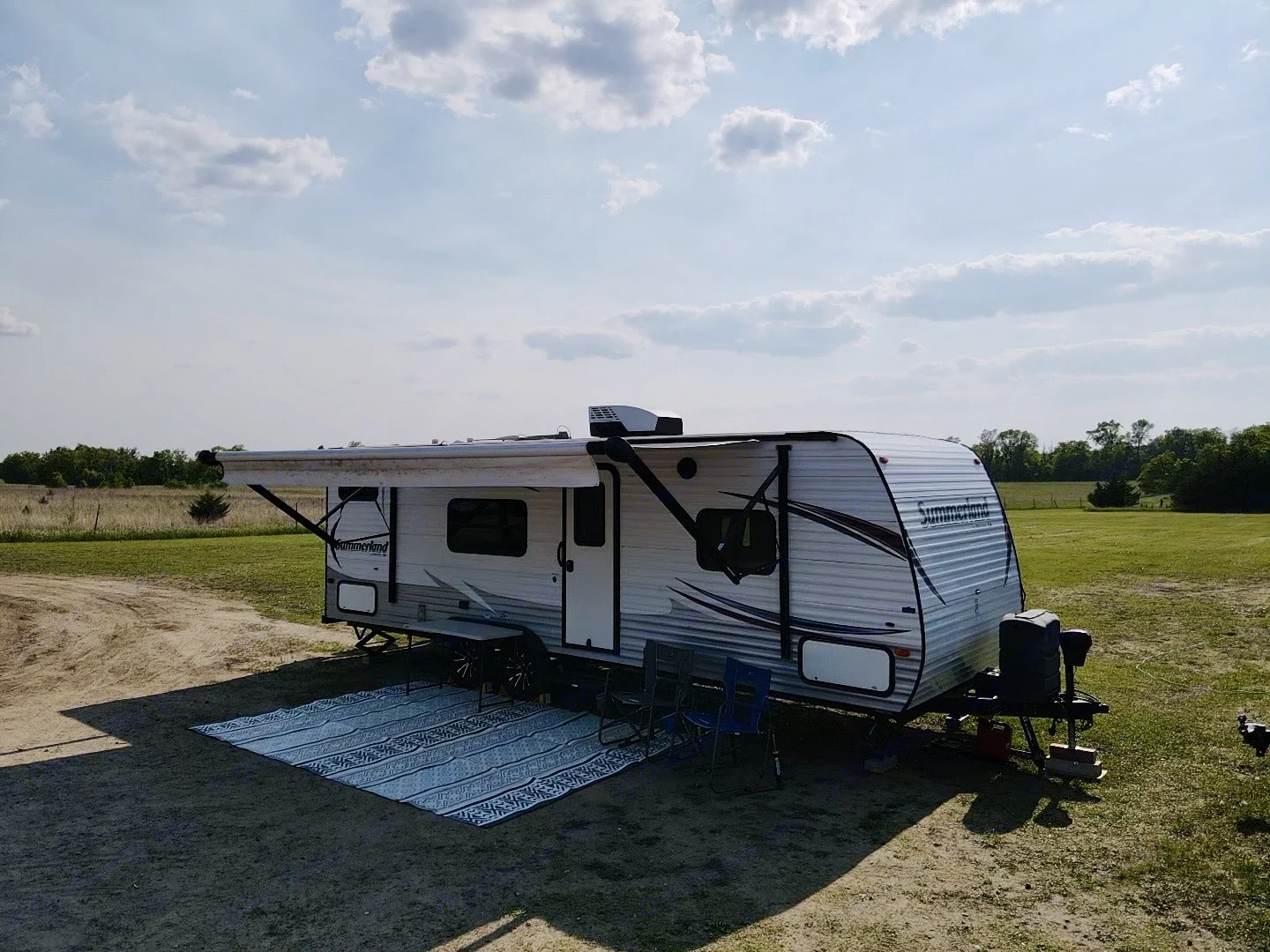Enjoy this RV rental setup: a travel trailer parked in a serene field with an extended awning and outdoor mat for relaxation.. Keystone RV Summerland 2015
