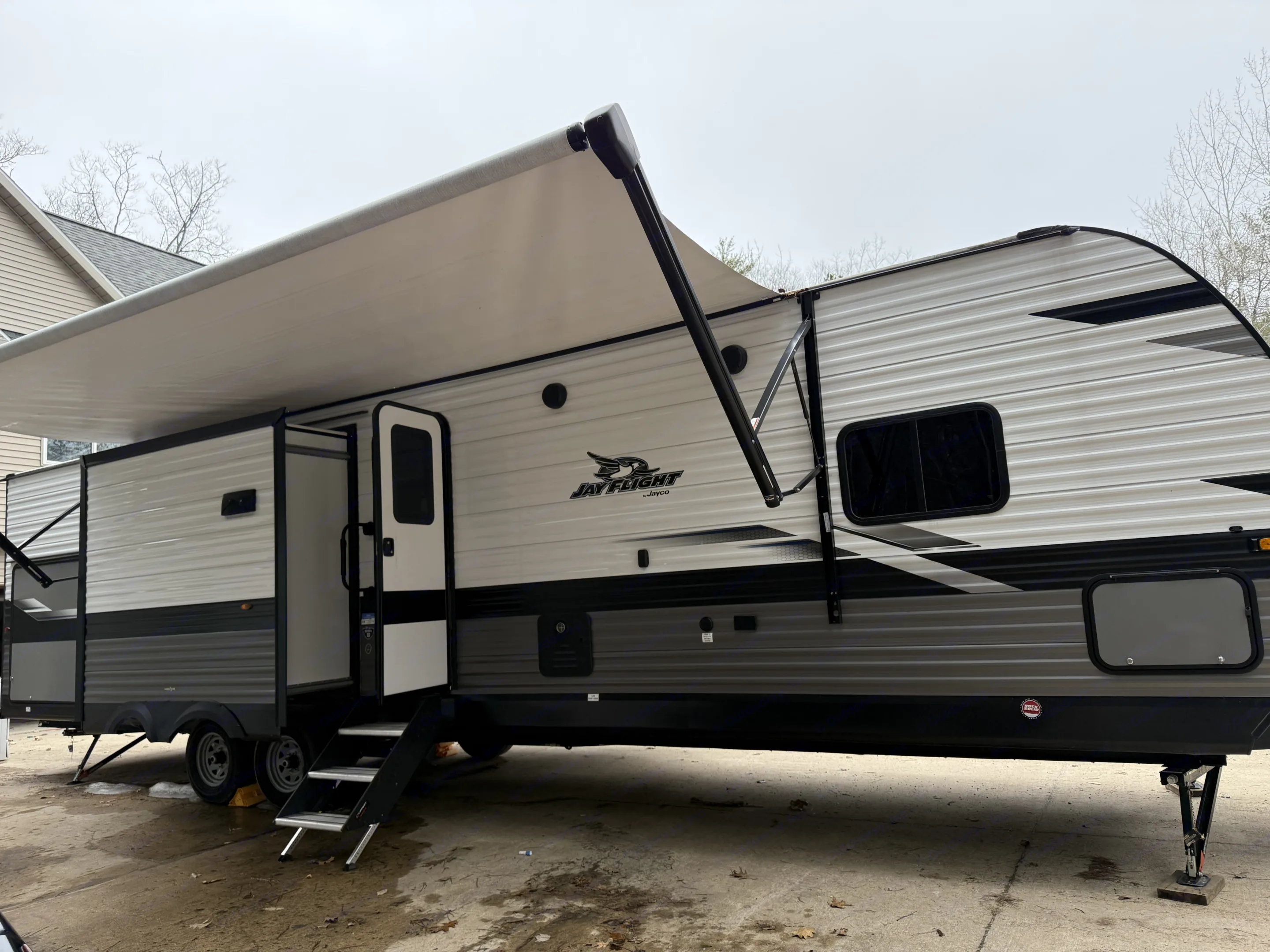 White and grey Jay Flight travel trailer with an extended awning and deployed steps, ready for an RV rental or camping trip.. Jayco Jay Flight 2023