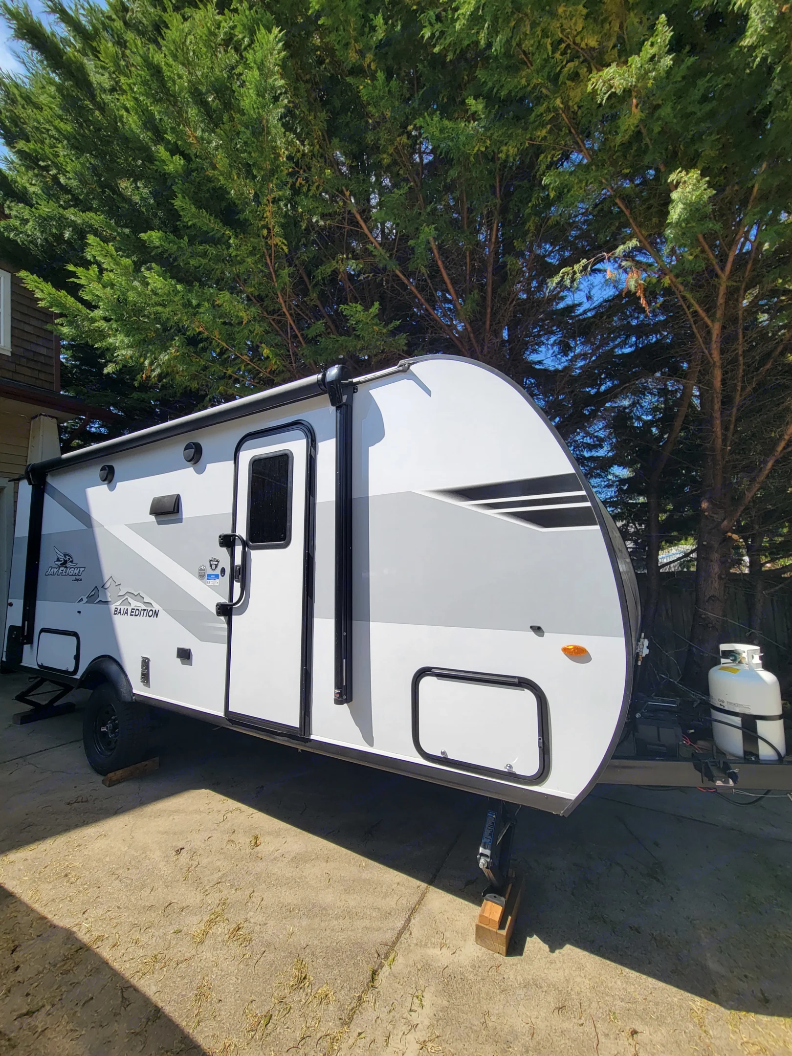 This white Jayco Baja Edition rv rental travel trailer is parked on concrete, shaded by lush green trees.. Jayco Jay Flight SLX 197MBW Baja Edition 2025