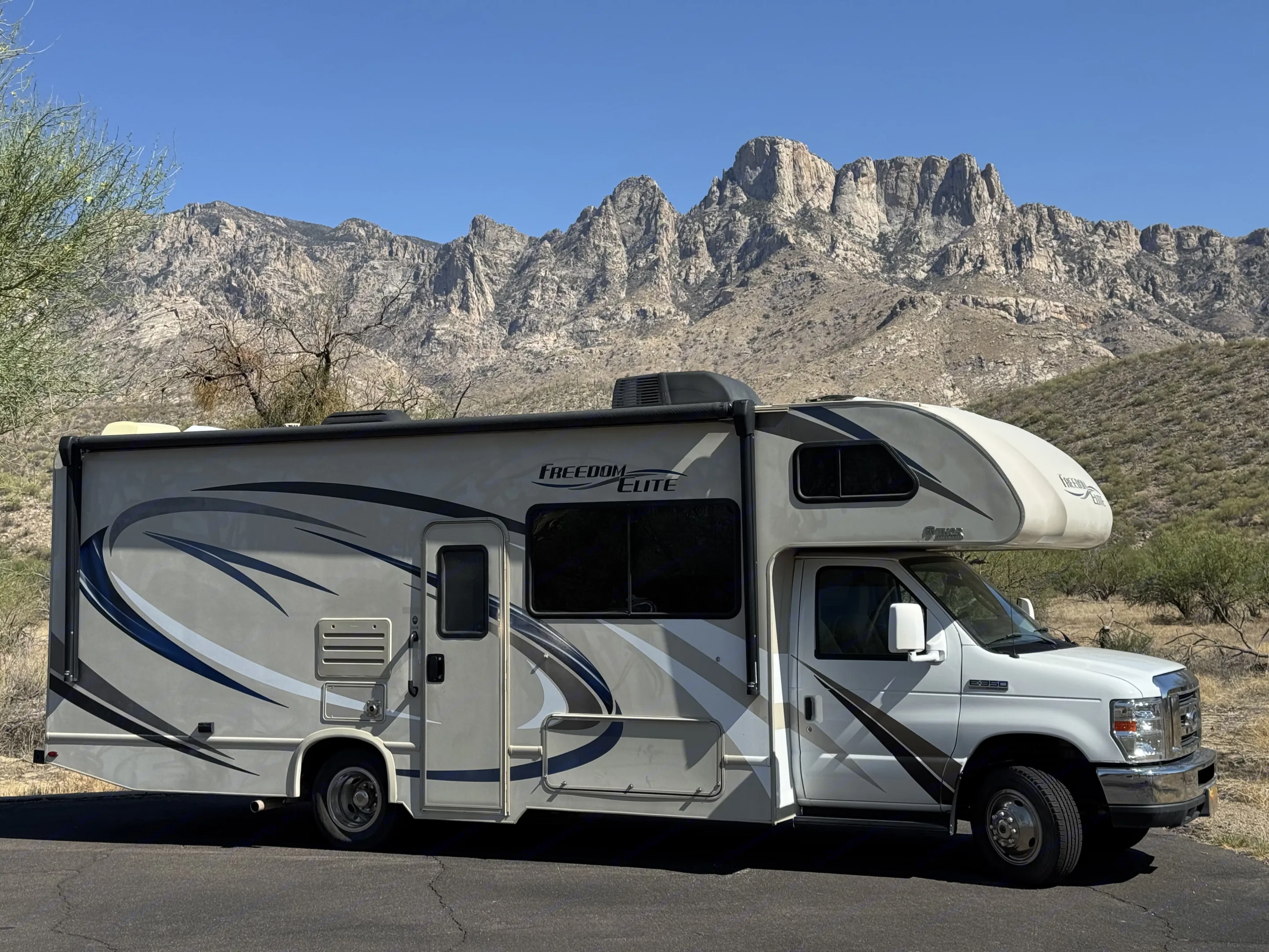 Freedom Elite rv rental parked with rugged mountains under a clear blue sky. Ideal for scenic adventures.. Thor Freedom Elite 2019