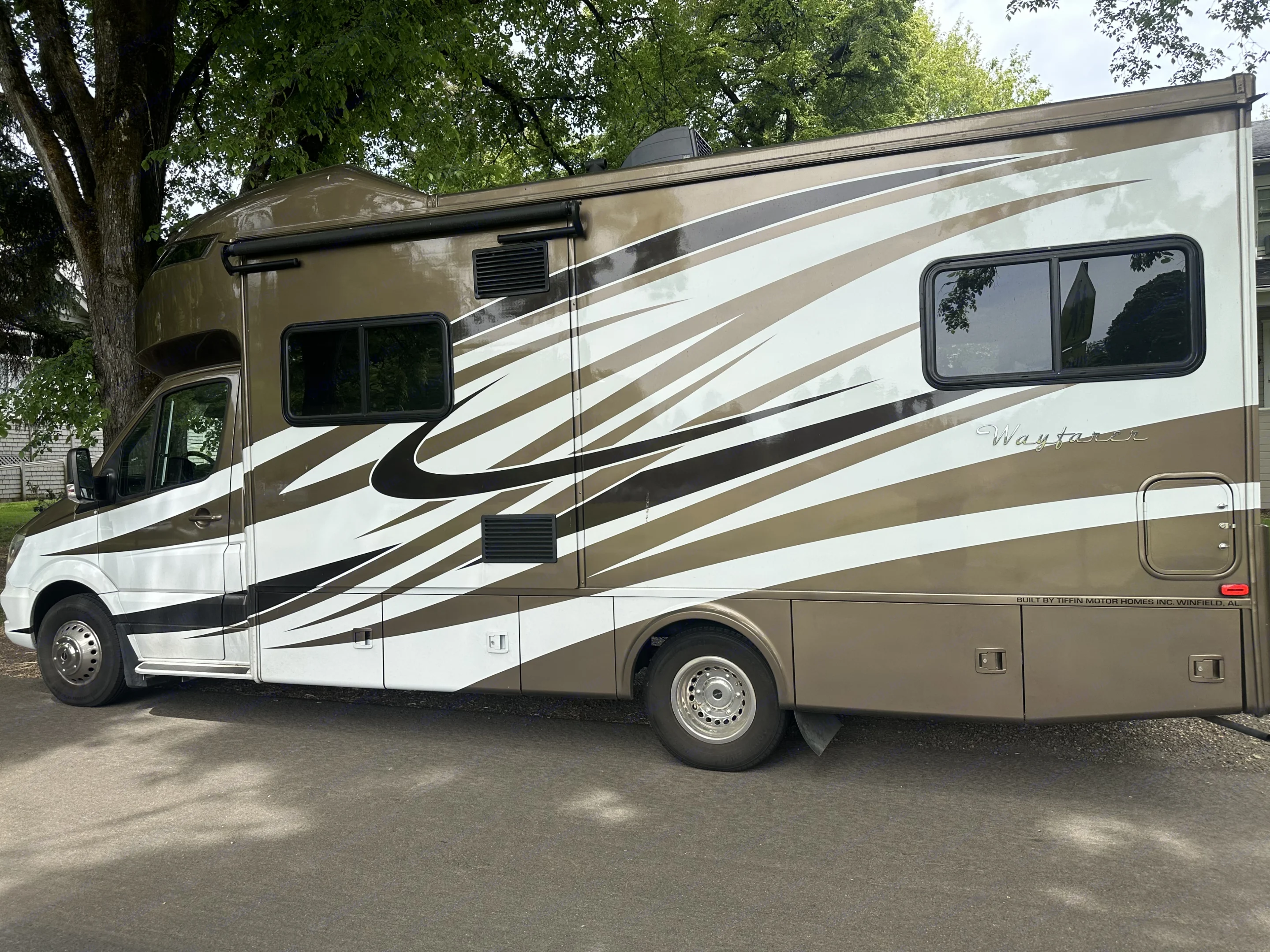 This sleek brown & white Tiffin Wayfarer RV rental is a premium motorhome parked under lush trees.. Wayfarer Wayfarer Motorhome 2018