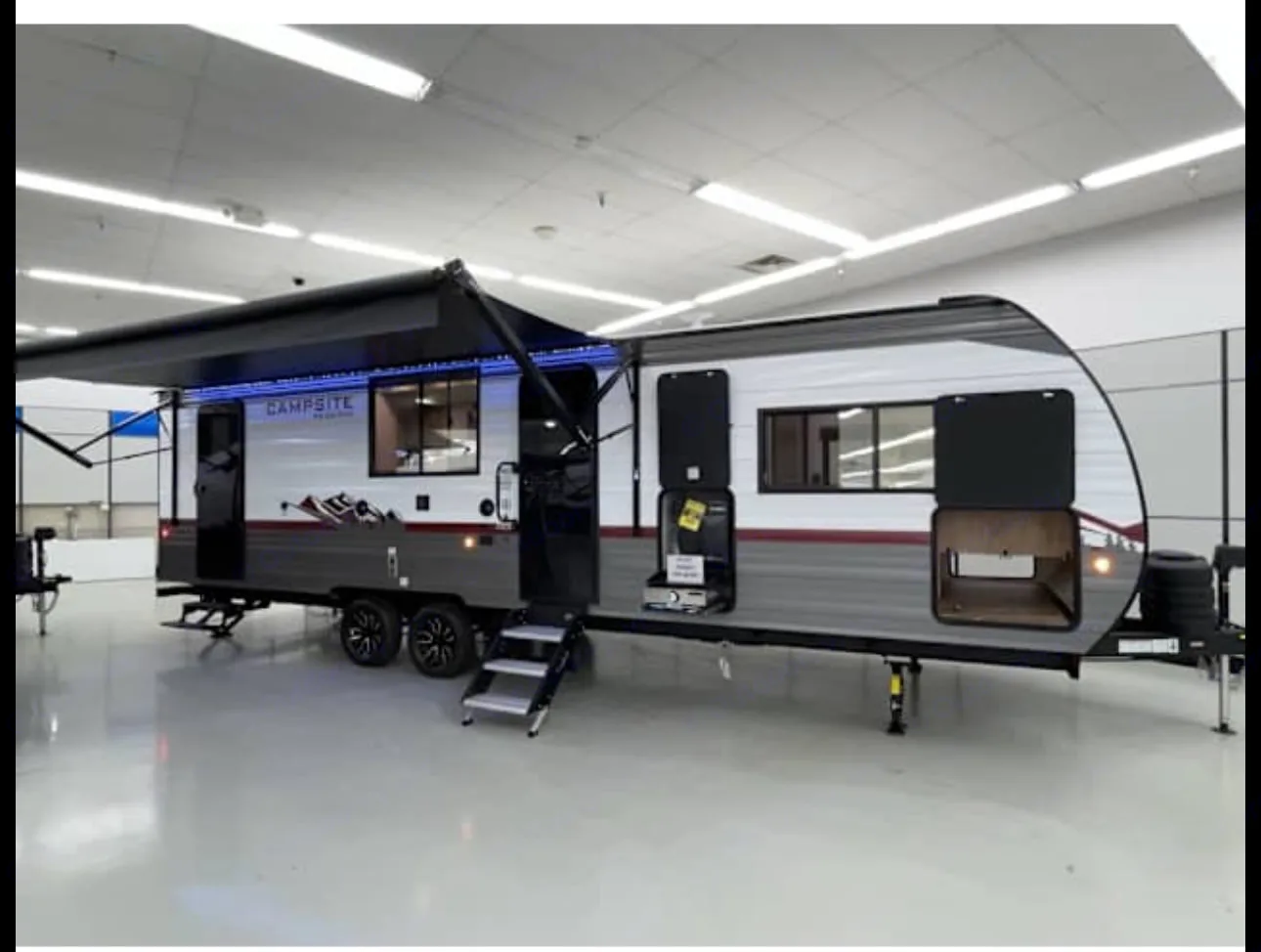 This Campsite travel trailer, ideal for RV rental, displays its extended awning with blue LEDs, steps, & open storage.. Forest River Campsite Reserve 26CJ 2025