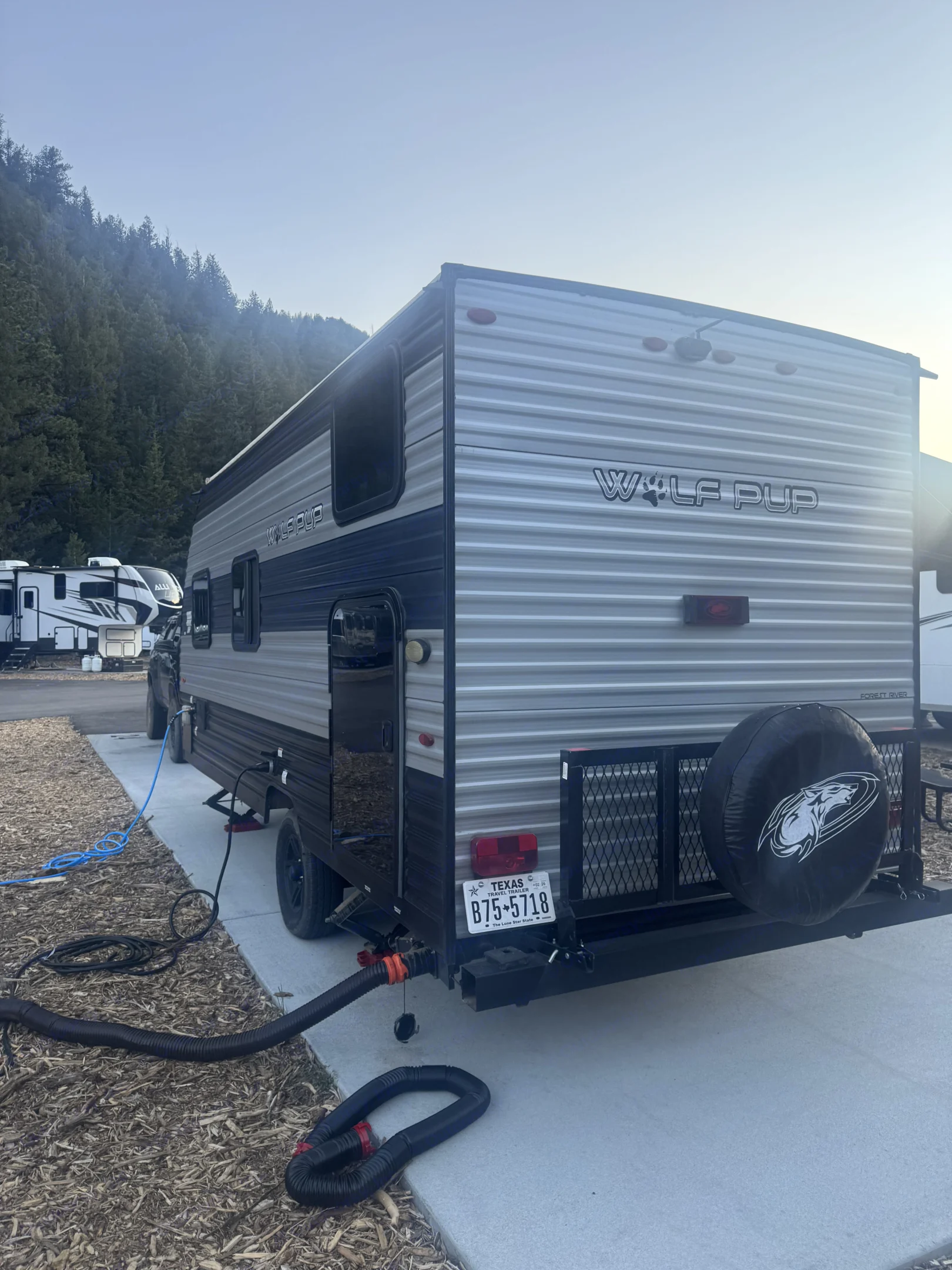 A Wolf Pup travel trailer (RV) is set up at a scenic campground. Hoses are connected, perfect for an rv rental adventure.. Forest River Cherokee Wolf Pup 2022