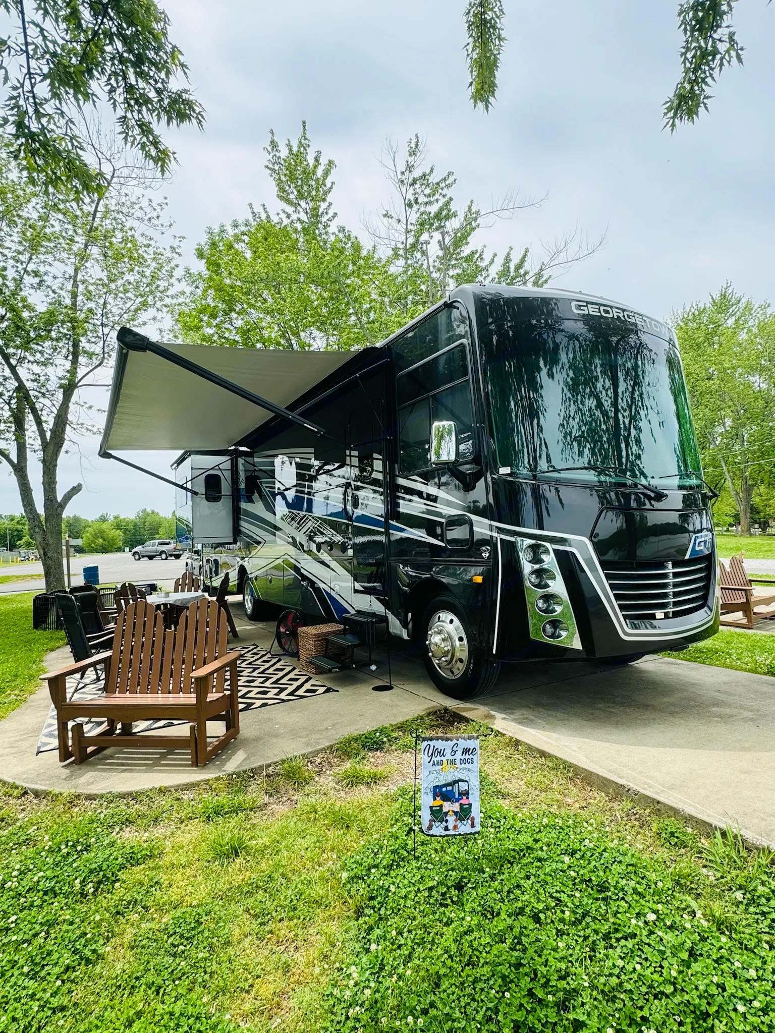 A sleek black RV rental is perfectly parked at a campsite, featuring an extended awning & comfortable outdoor furniture for relaxing.. Georgetown GT7 2024