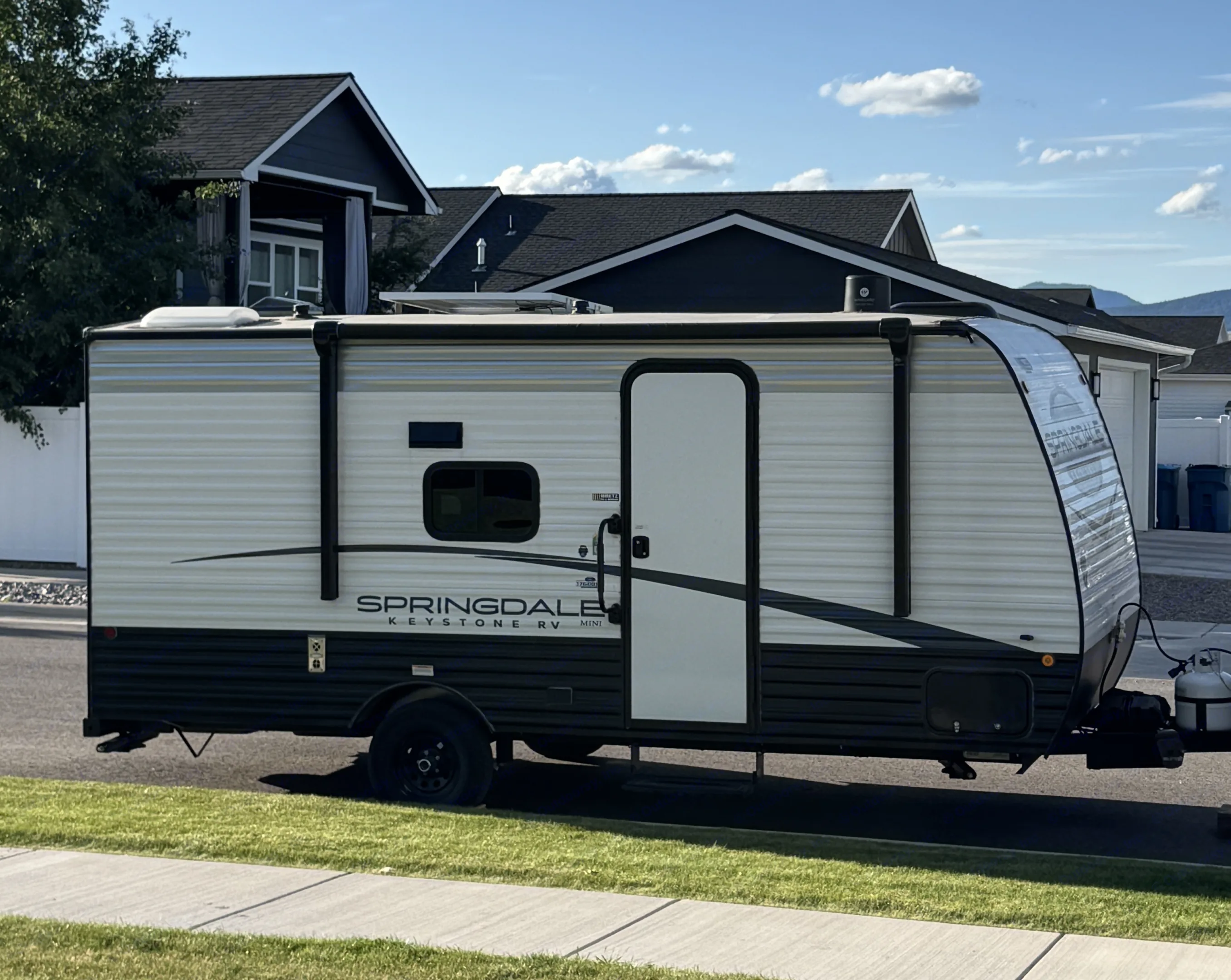 A Springdale Keystone Mini travel trailer, ideal for an rv rental, parked on a sunny street beside houses. Ready for adventure!. Keystone RV Springdale 2024
