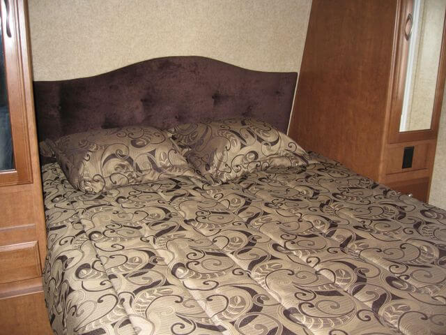 A cozy RV rental bedroom featuring a patterned bed, dark headboard, and wood cabinetry with a mirrored closet.. Eclipse Milan 2011