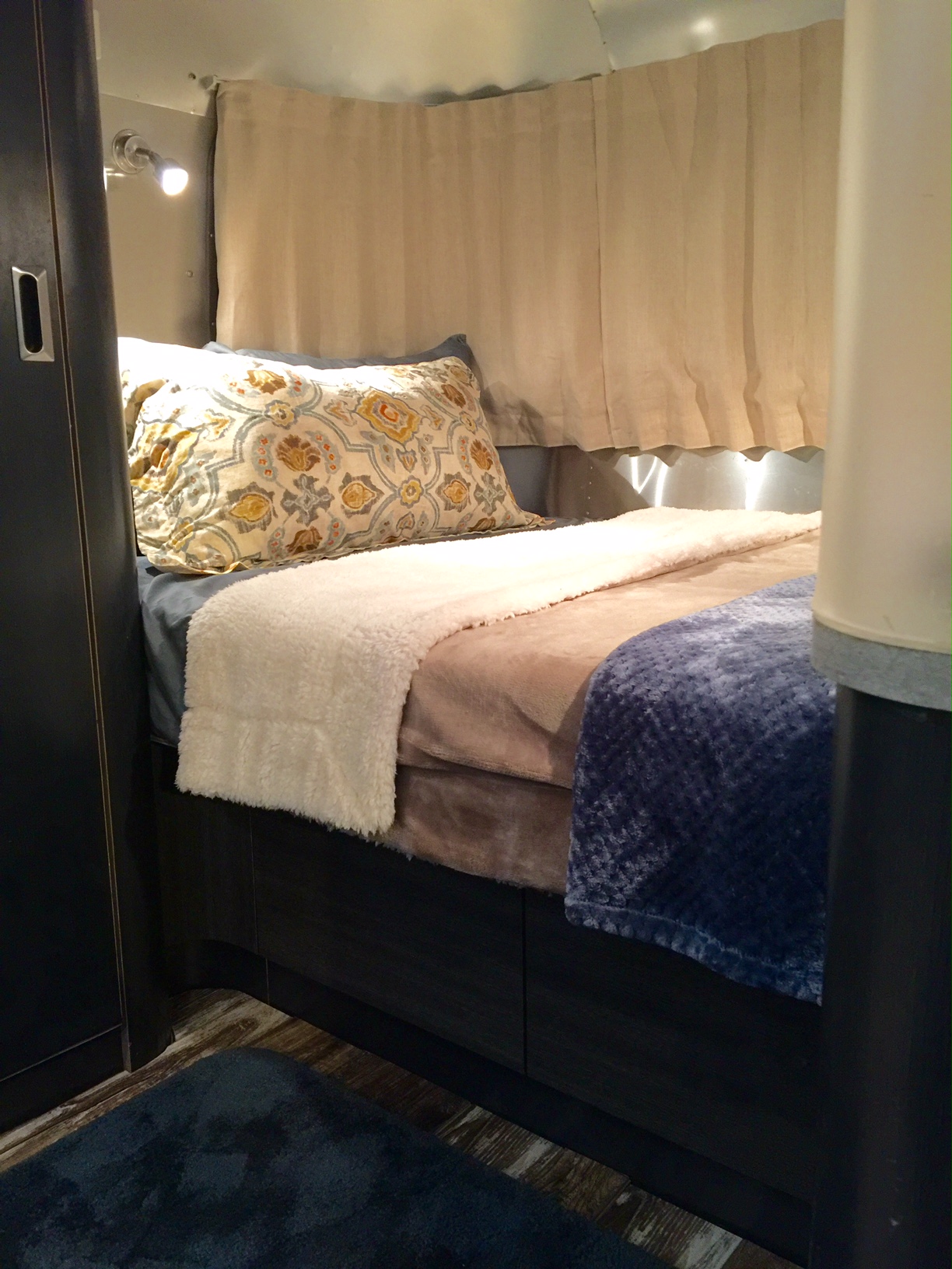 Cozy bed inside an RV rental, with a patterned pillow, soft white and blue blankets, and warm lighting. Perfect for relaxing travel.. Airstream International 2003
