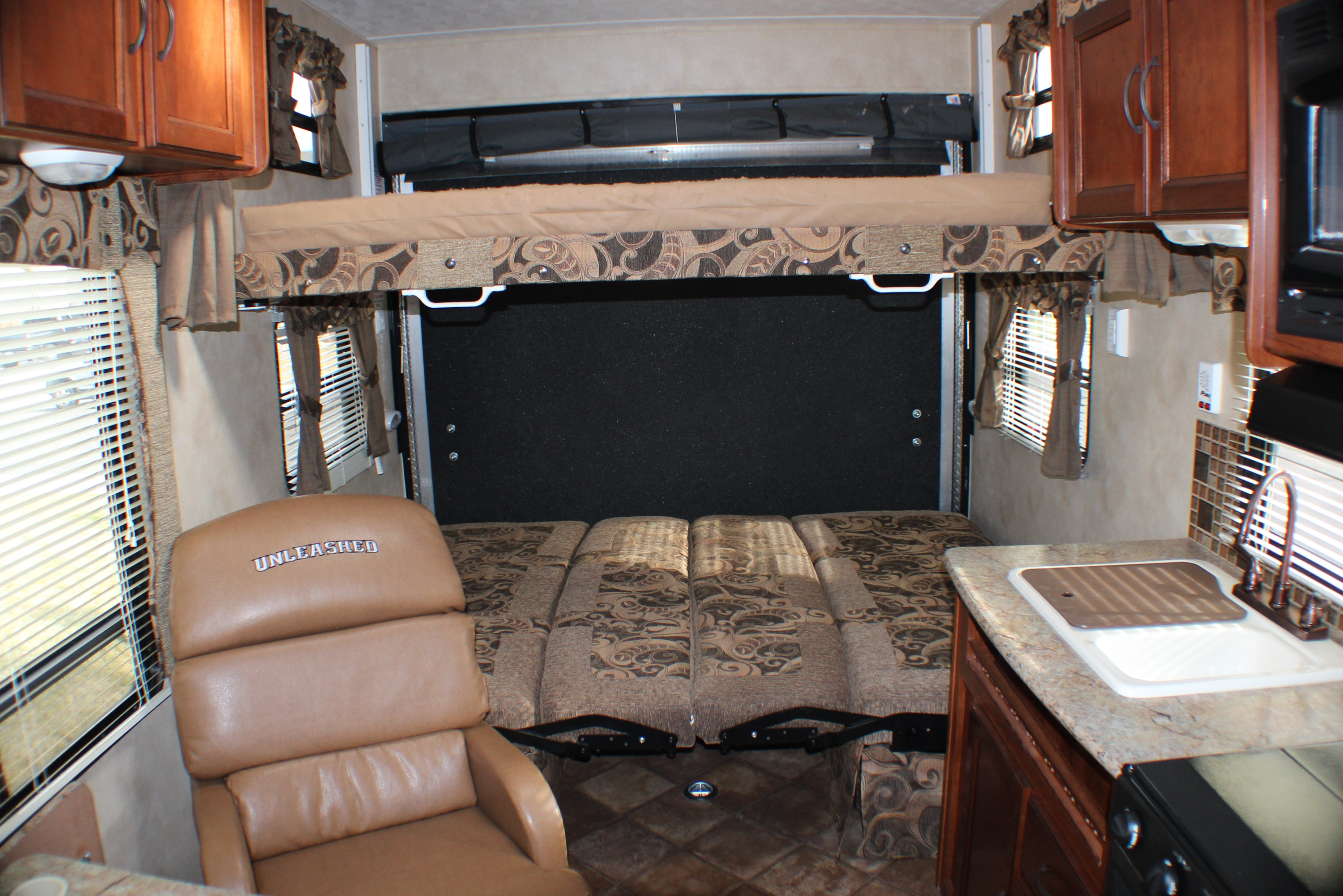 RV rental interior with convertible bunk beds (upper raised, lower seating/bed), 'UNLEASHED' recliner, and kitchen with sink.. Palomino Puma Unleashed 2013