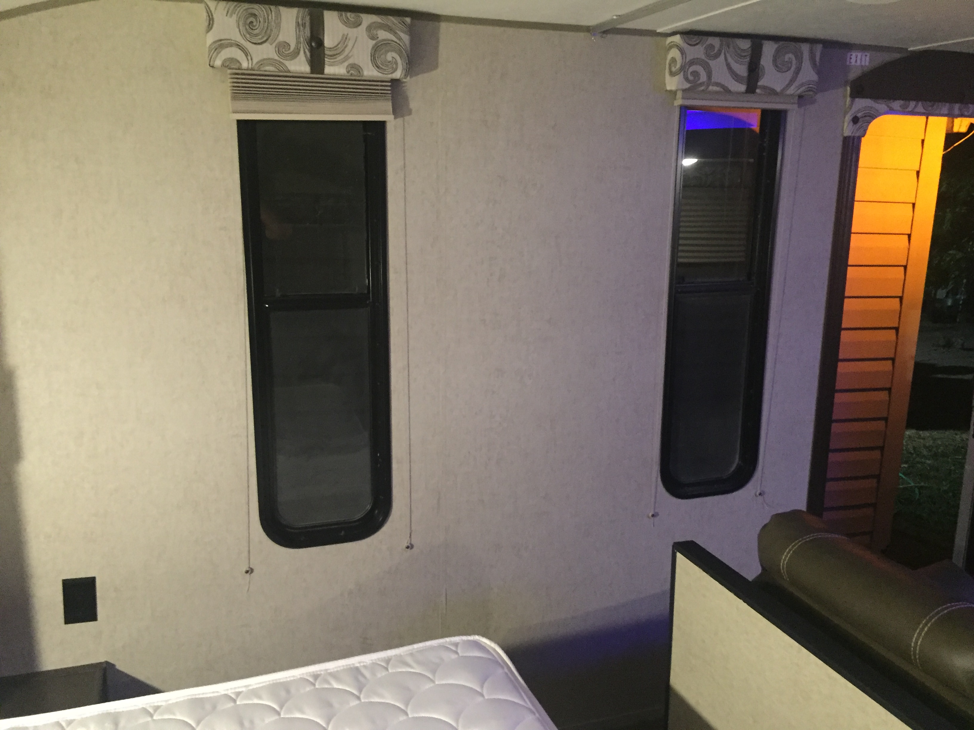 Inside an RV rental, showing two windows with blinds, a white mattress, and textured walls, typical of a travel trailer bedroom.. Forest River Cherokee Grey Wolf 2016