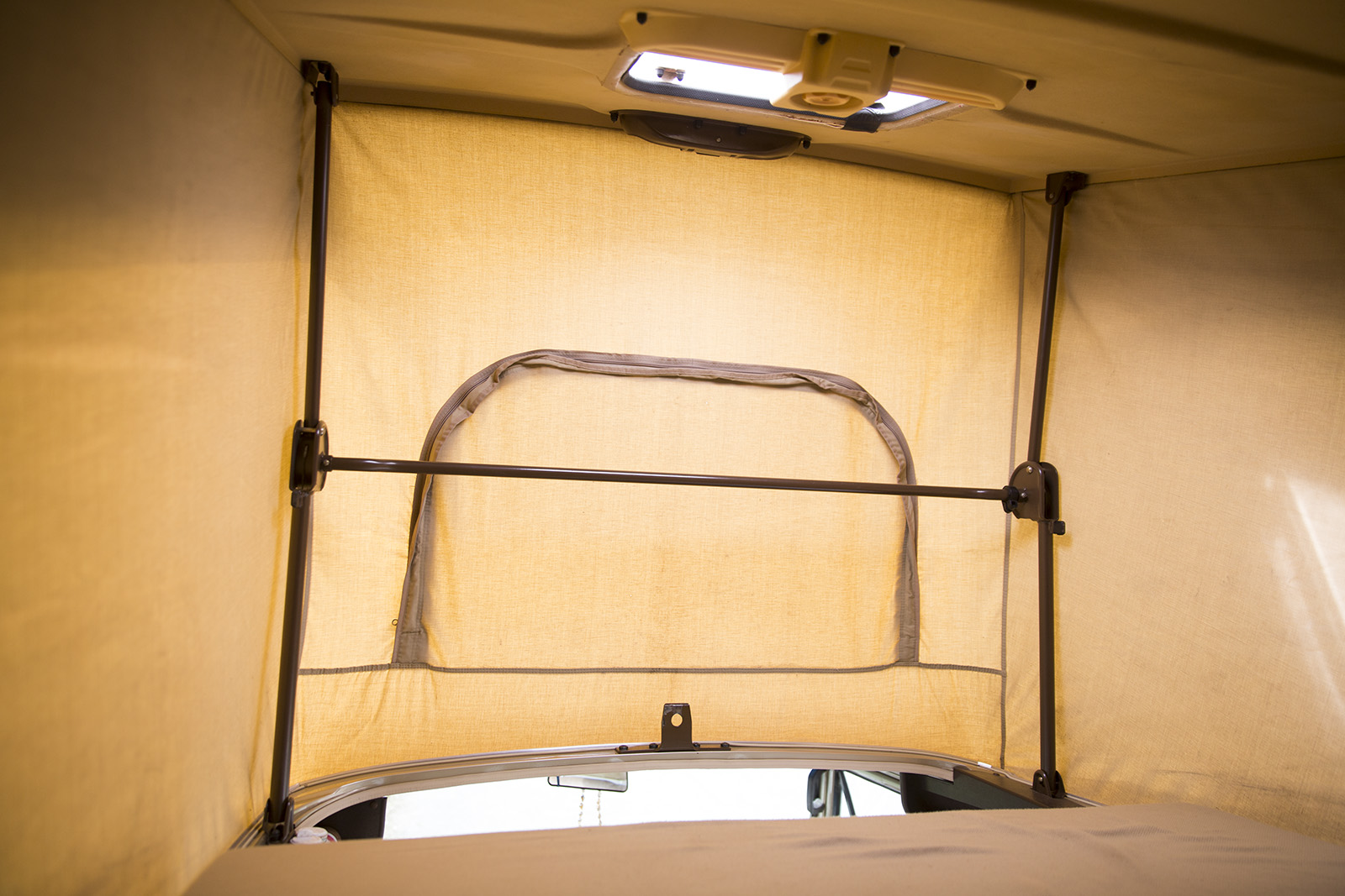 View inside an RV rental pop-top camper, featuring light fabric walls, support poles, a zippered opening, and overhead vent.. Volkswagen Vanagon 1983