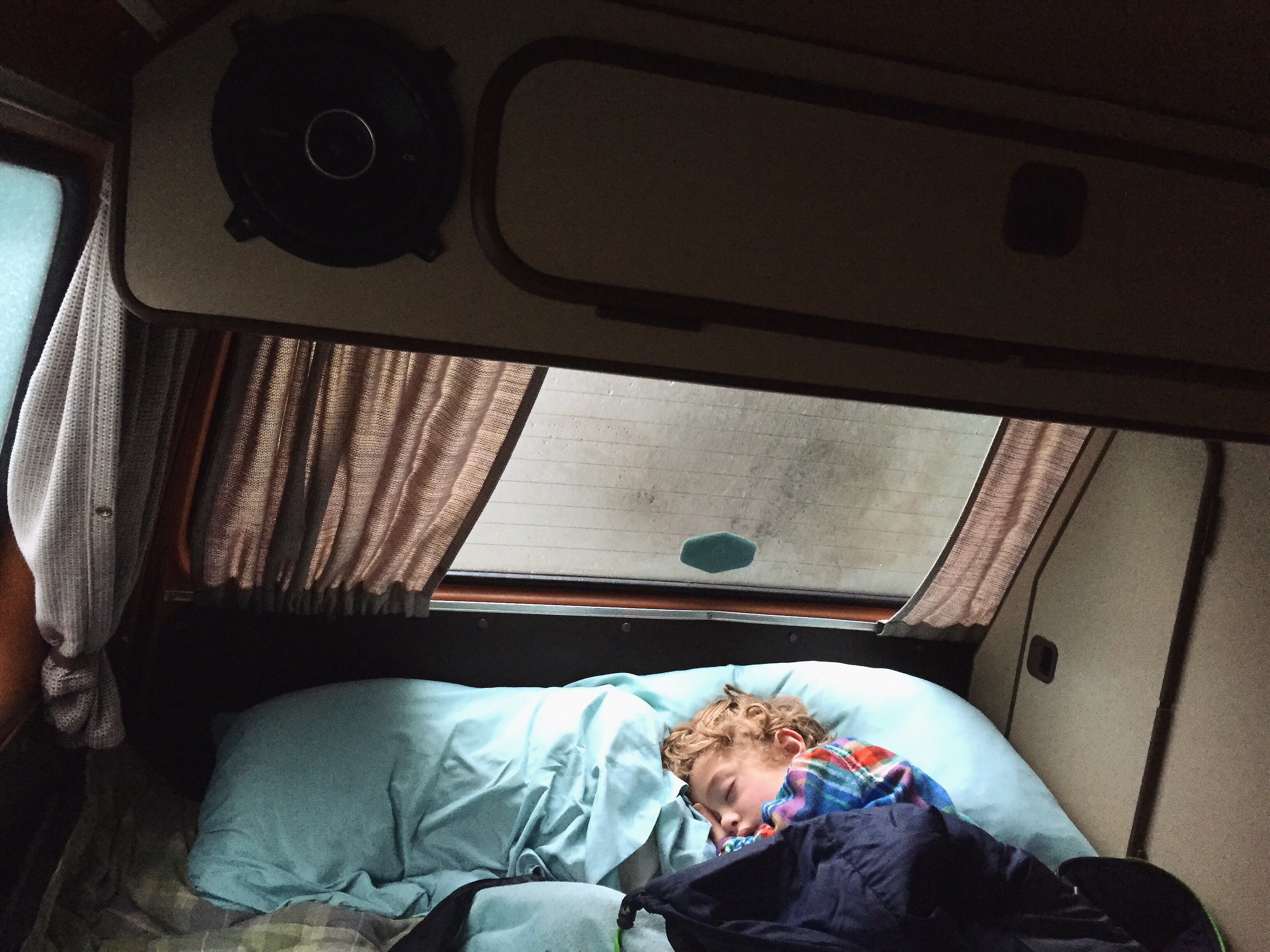 A child peacefully sleeps in a cozy RV rental bed, nestled inside a camper van with curtains & speaker visible, perfect for travel.. Volkswagen Vanagon 1985