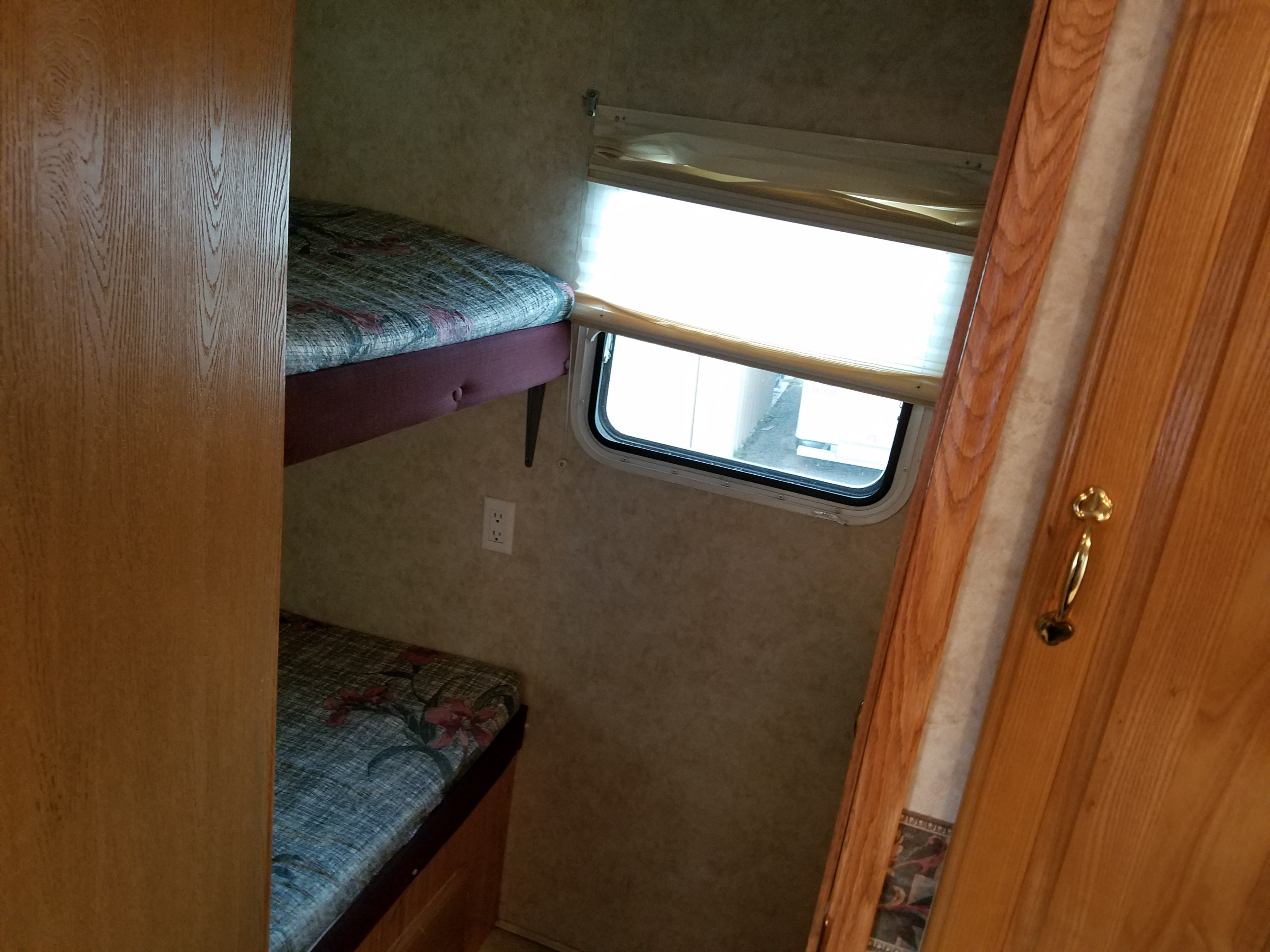 RV rental interior: two stacked bunk beds with blue/red patterned mattresses, a window with light blinds, and a white wall outlet.. Forest River Cedar Creek Silverback Edition 2005