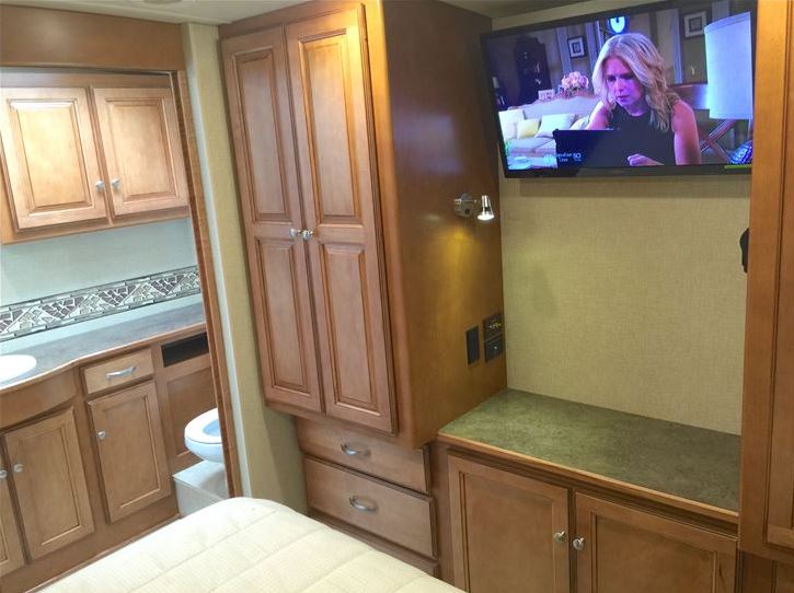 Well-appointed RV rental interior: bedroom with TV, ample built-in storage, and glimpse of the functional bathroom.. Itasca Sunstar LX 35F 2016