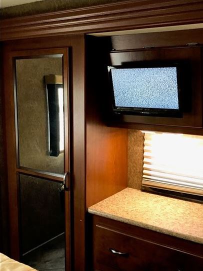 RV rental bedroom with dark wood trim, a TV, mirrored closet door, and granite-look counter/drawers for storage.. THOR A.C.E 30.2 2015