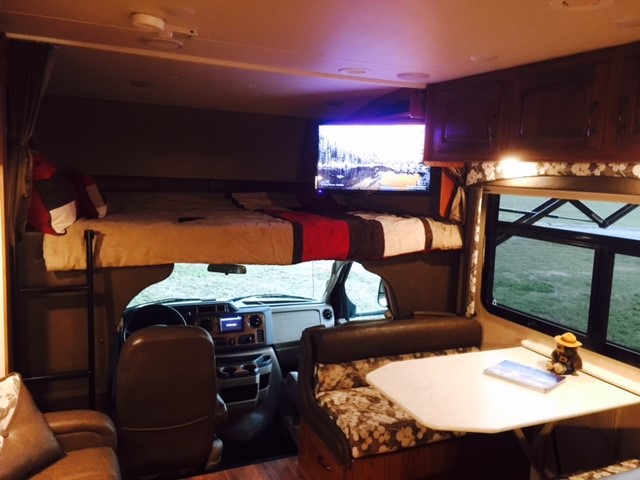 Comfortable RV rental interior featuring an overhead bed, dining table, driver's cockpit, and lounge area for your journey.. Jayco Greyhawk 2016