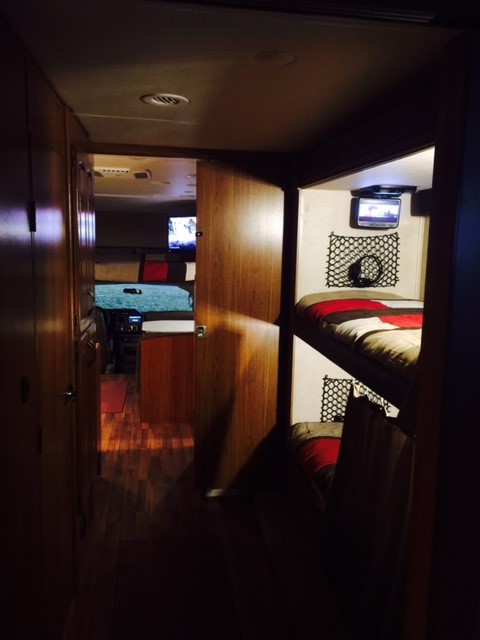 Cozy RV rental interior: bunk beds with TVs, wood flooring, and a spacious living area visible beyond.. Jayco Greyhawk 2016