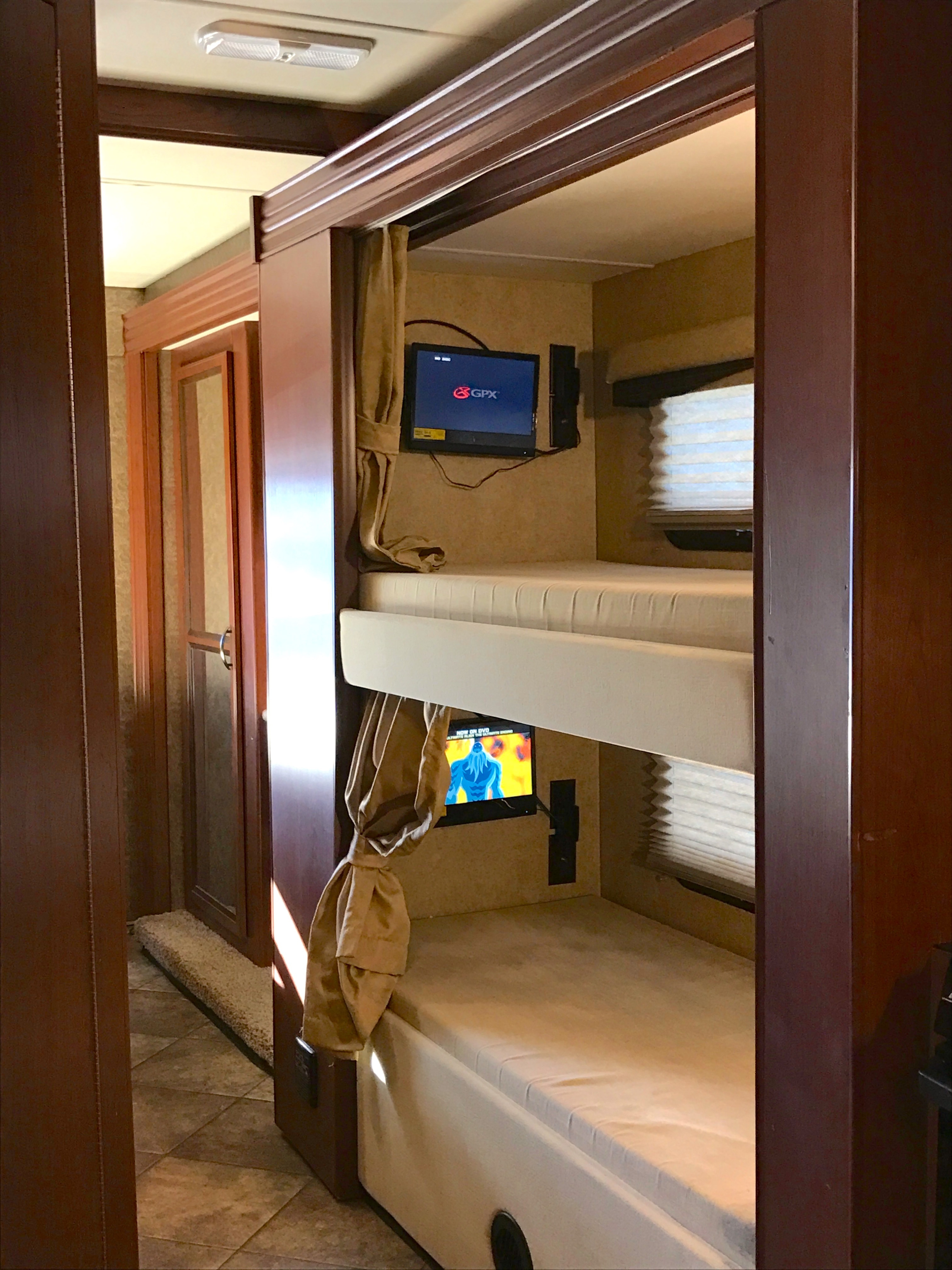 Inside an RV rental: a set of bunk beds, each equipped with its own small TV, blinds, and tied-back curtains.. THOR A.C.E 30.2 2015