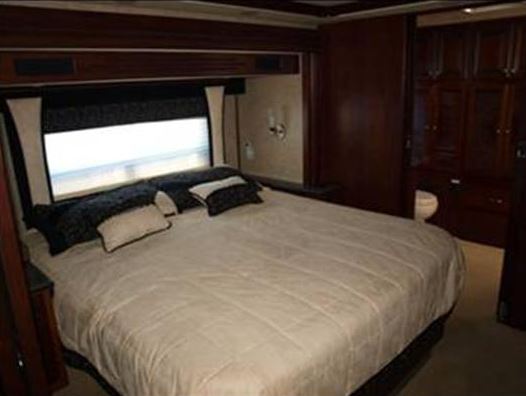 Luxurious RV rental bedroom with a comfy bed, large window, elegant wood interiors, and a peek at the en-suite bath.. Fleetwood Revolution
