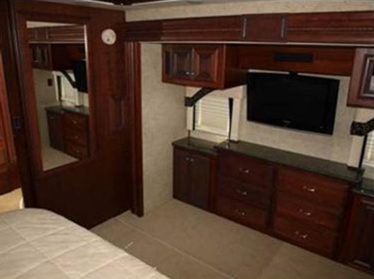 Experience comfort in this RV rental's bedroom, boasting dark wood cabinetry, a mounted TV, and convenient storage.. Fleetwood Revolution