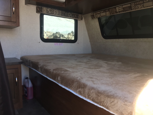 Cozy RV rental interior with a comfortable bed, windows offering views of a rocky landscape, and built-in storage.. Jayco Jayflight SLX 175XD 2017