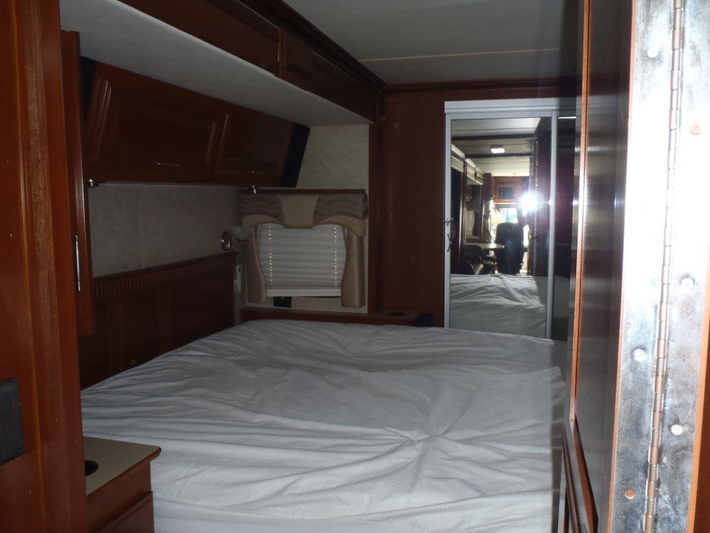 RV rental bedroom featuring a neat bed, overhead storage, and mirrored doors reflecting the motorhome's living space.. Fleetwood Discovery