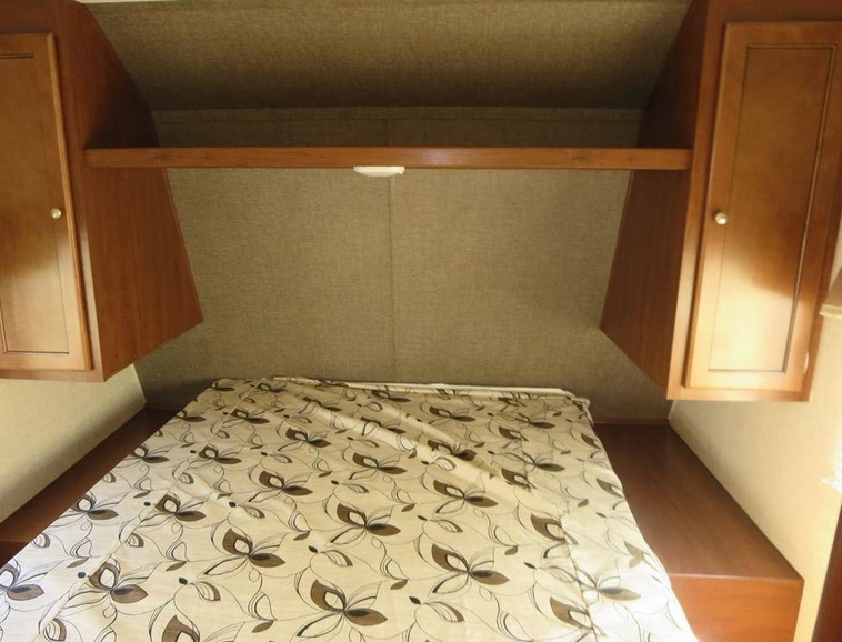 Cozy RV rental bedroom with patterned comforter, overhead cabinets, and shelf. Ideal for comfortable travel.. Heartland Trail Runner 2016