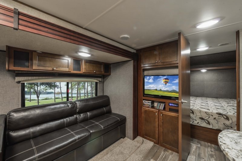 Spacious RV rental interior: living area with dark sofa, TV, built-in storage, and a separate bedroom.. Heartland Trail Runner 2017