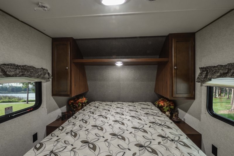 Cozy bedroom in an RV rental, featuring a patterned bed, storage cabinets, and scenic window views.. Heartland Trail Runner 2017